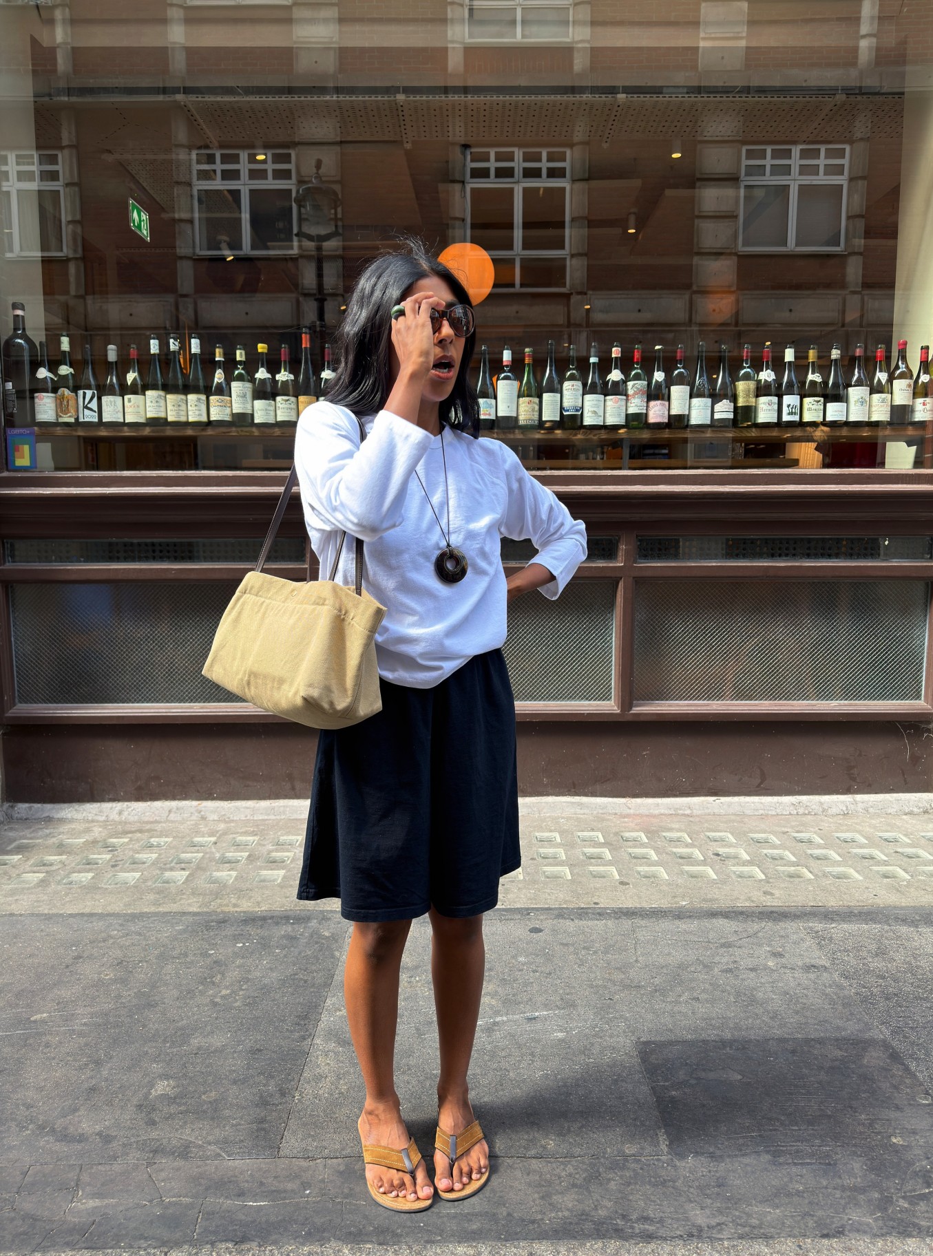An image of @monikh wearing a white long-sleeved shirt with black shorts and The Row flip-flops.