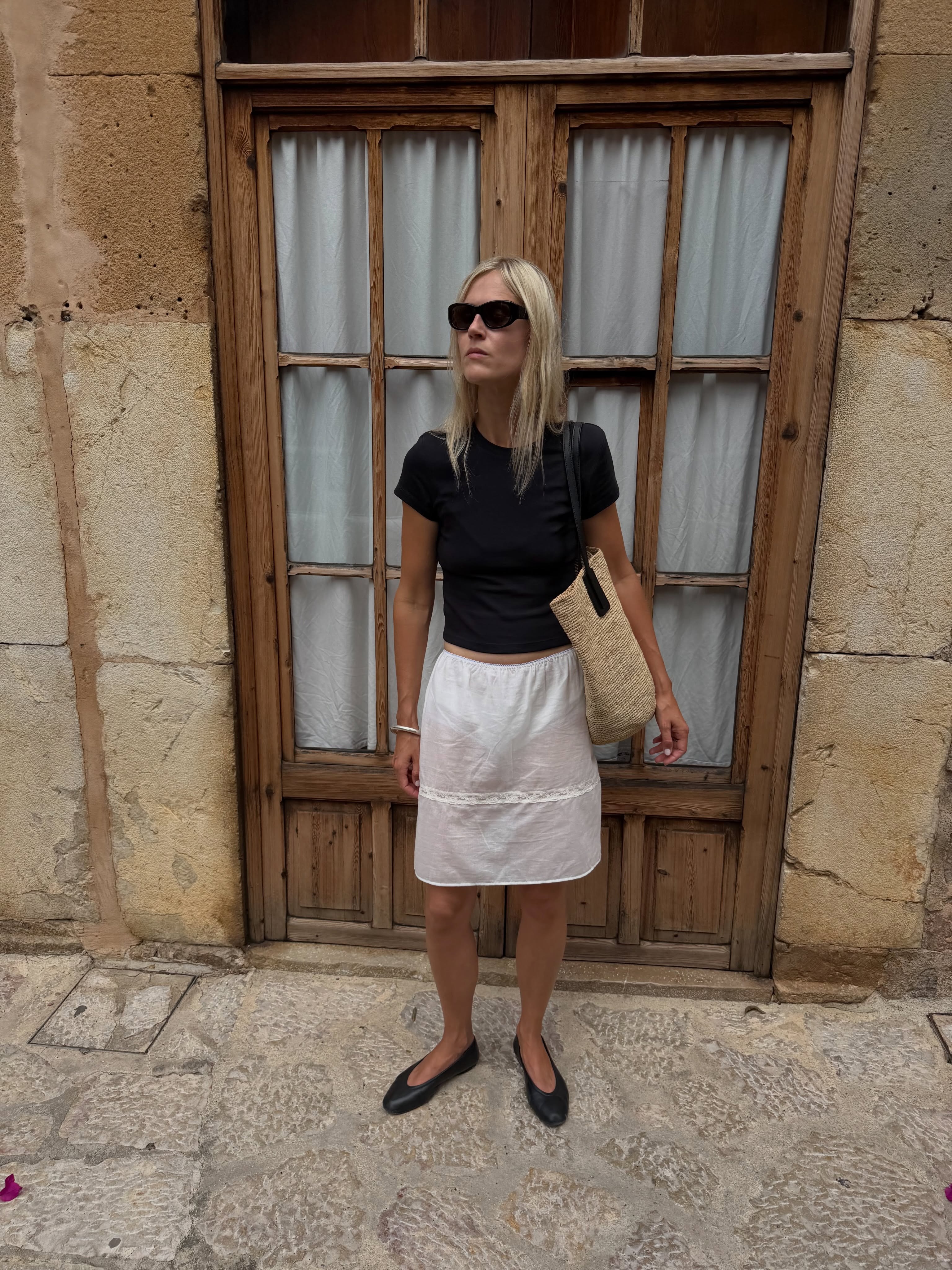 Woman in a black tee, white skirt and black ballet flats