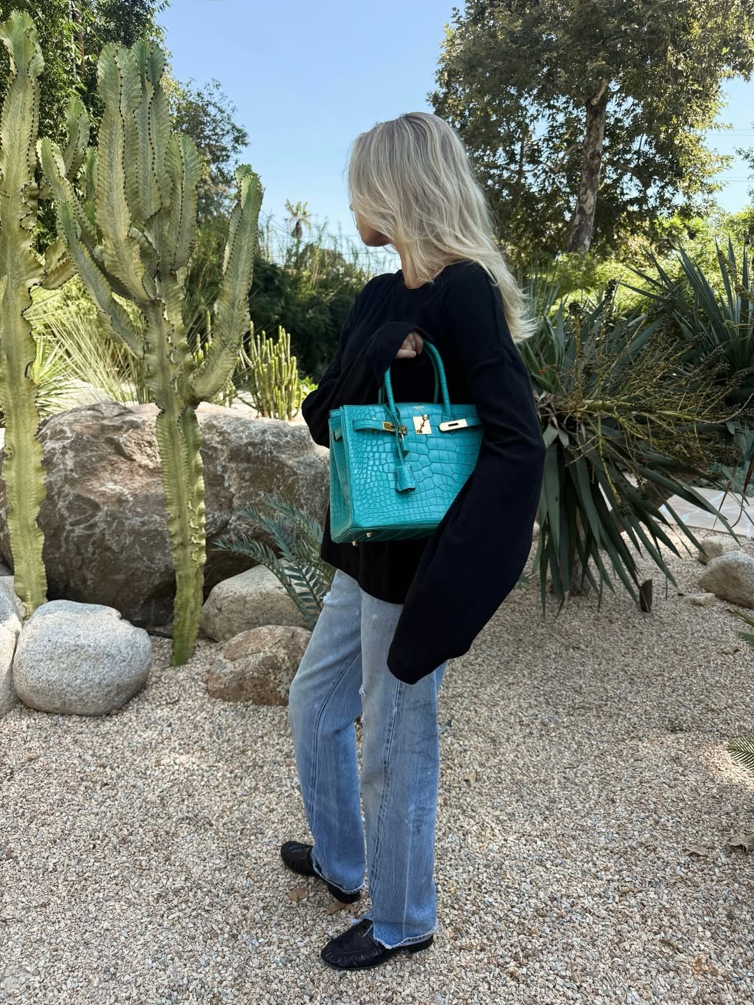 Model Elsa Hosk poses for a photo wearing a black jumper with straight-leg jeans, black loafers and a turquoise handbag.