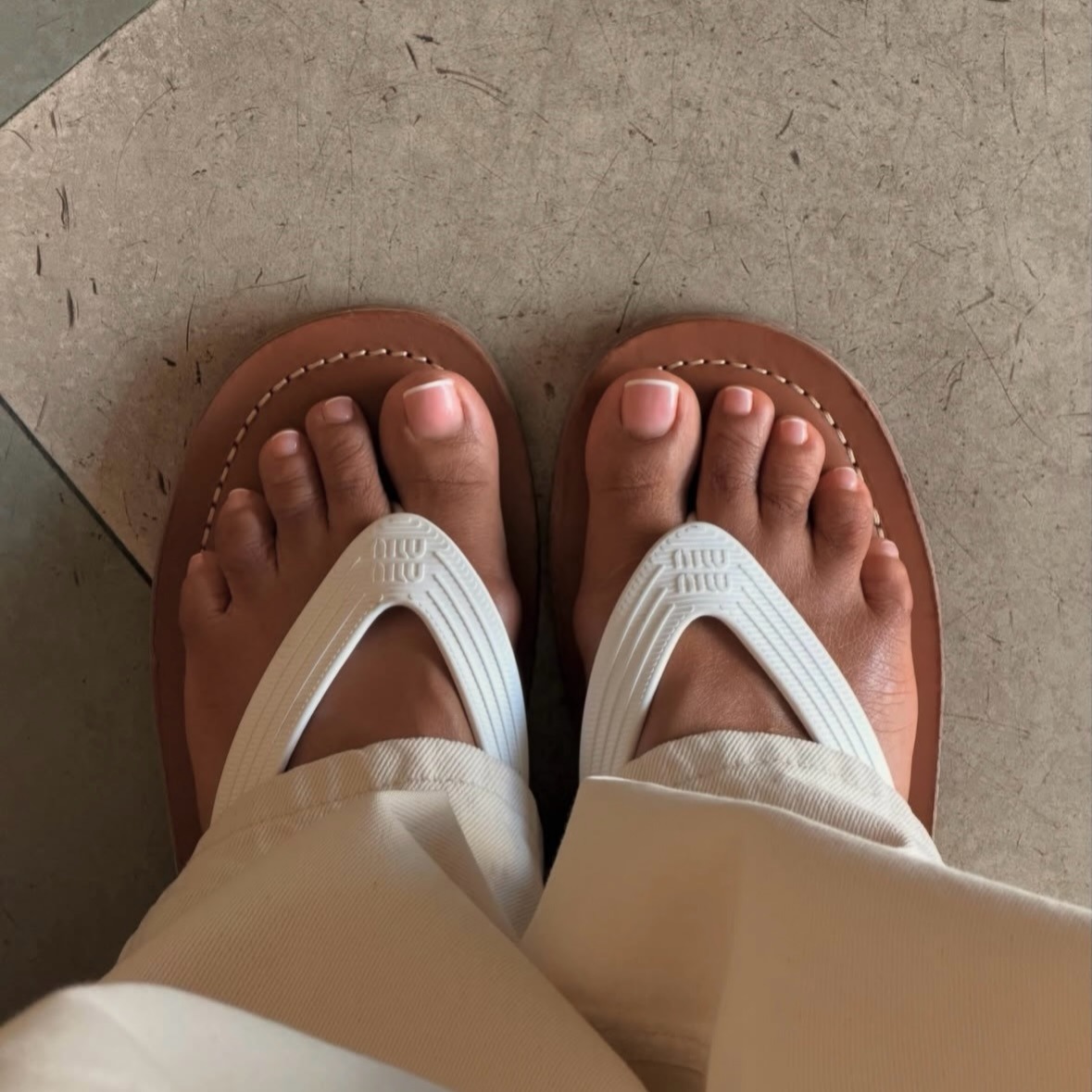 A close-up of feet in Miu Miu flip flops, with a French pedicure