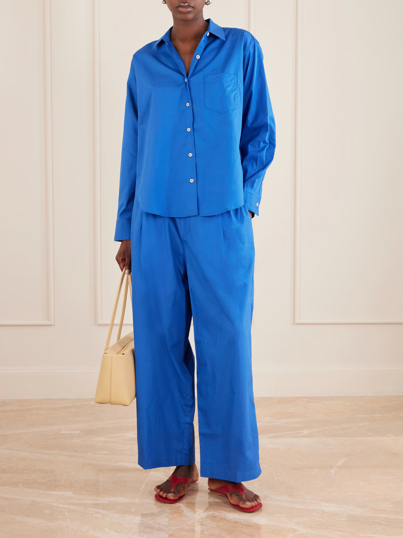 An image of a model wearing cobalt blue cotton poplin trousers with a matching top and red flip-flops
