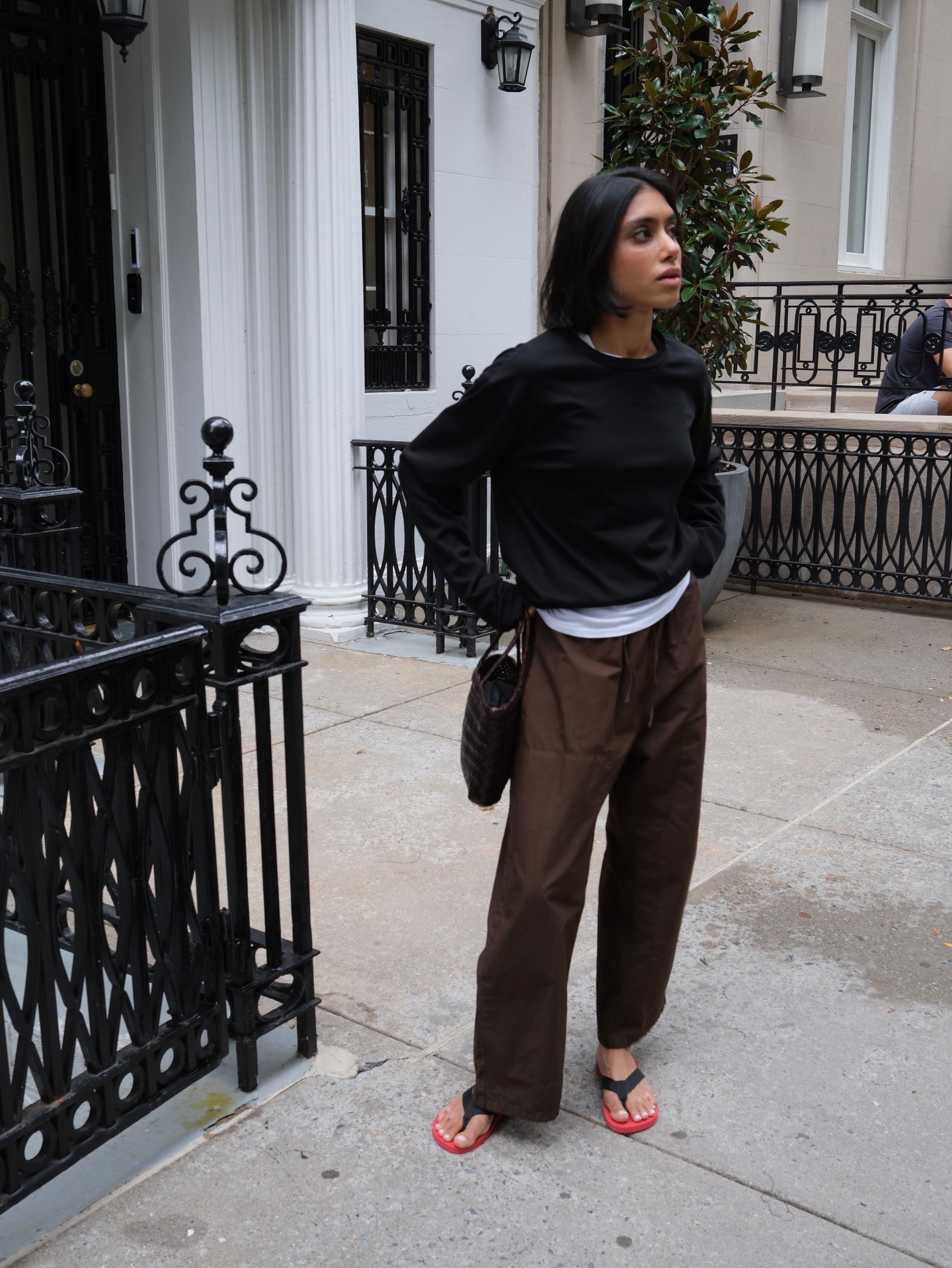 Shay wears a black sweater with a white tank top, brown j.crew luna pants, and black-and-red flip-flops.