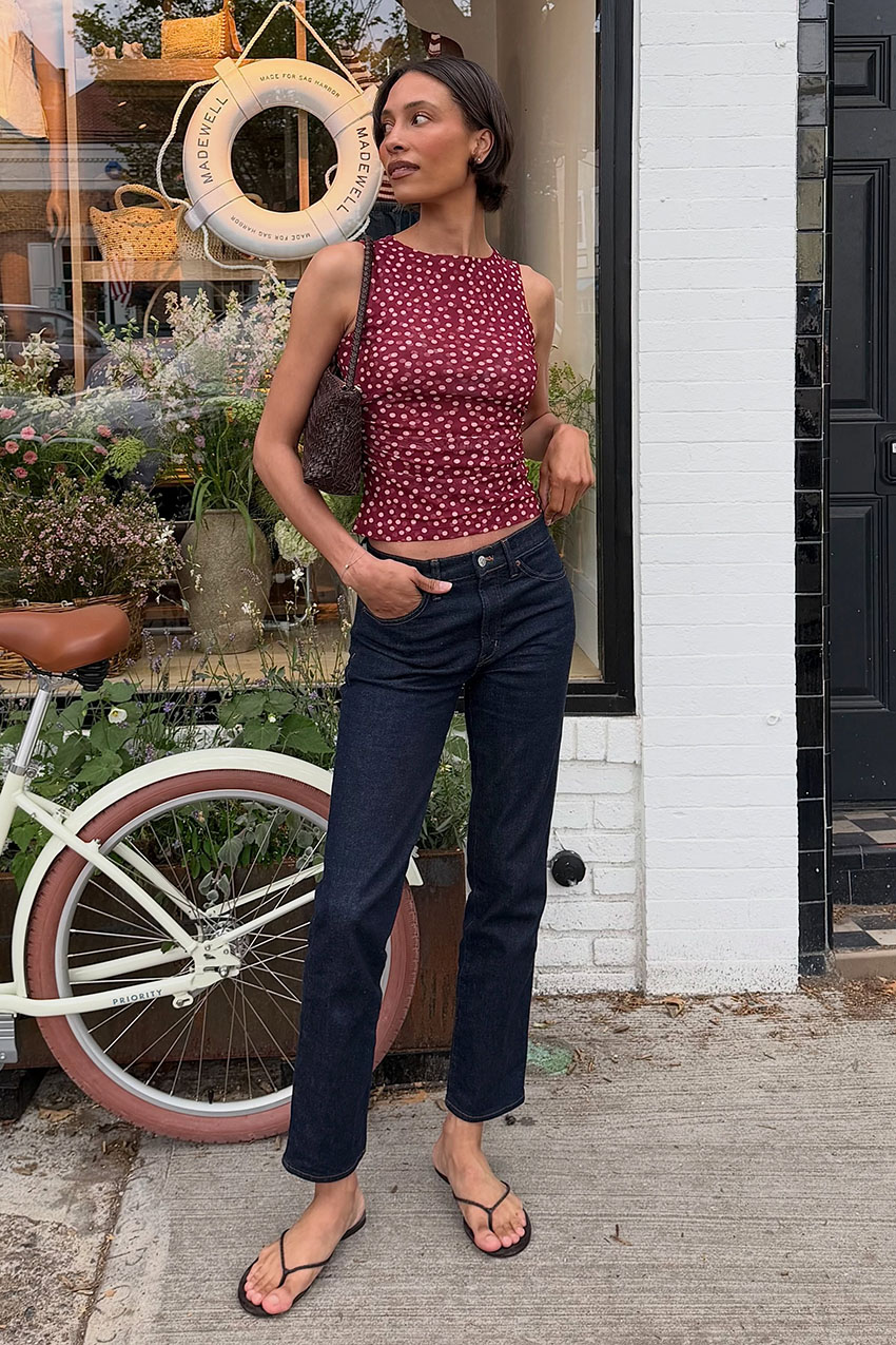a woman wearing a red polka dot tank top, dark wash jeans, and black flip flops