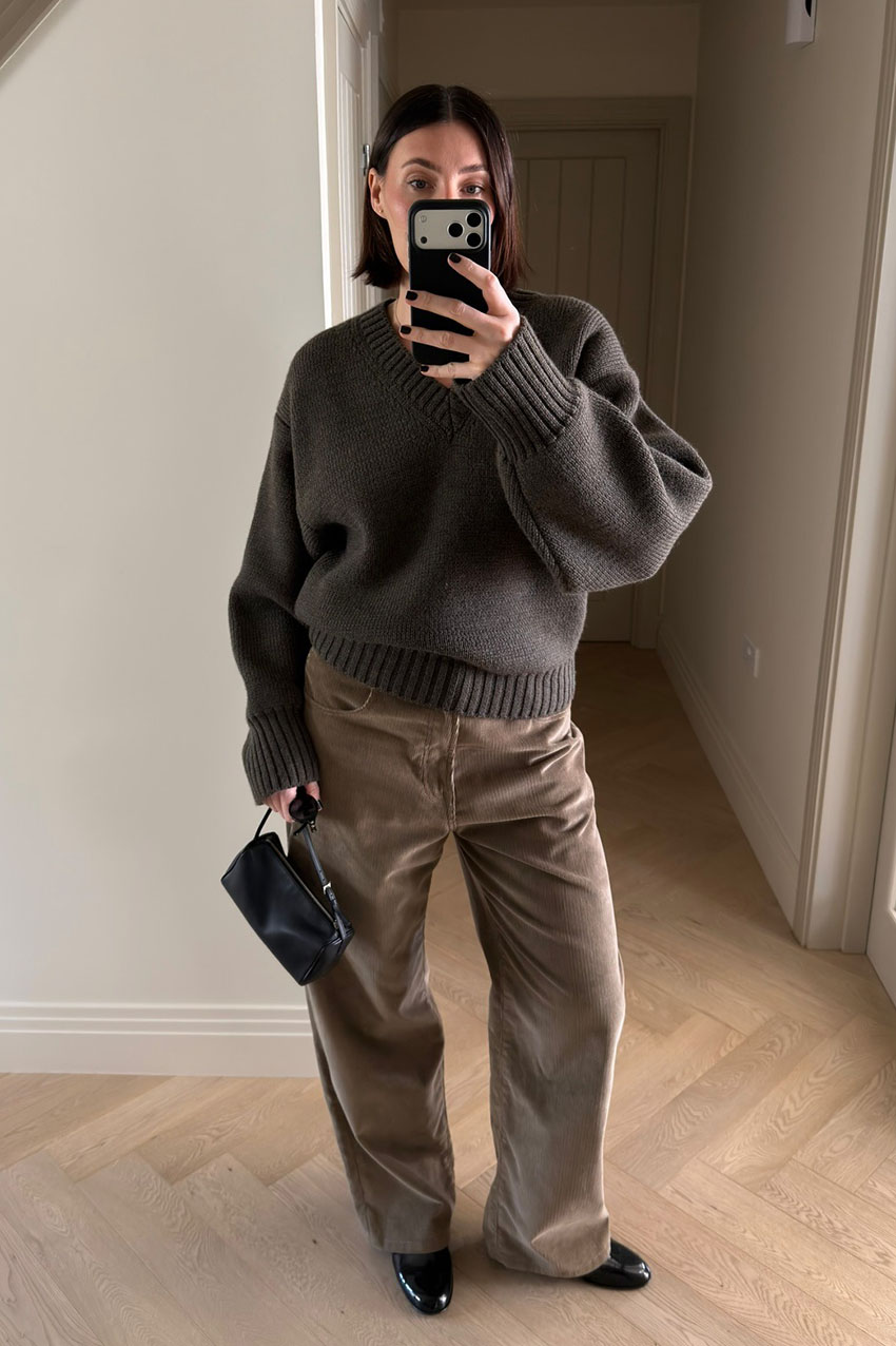 A woman wearing a brown sweater, brown barrel jeans, black boots, and a black bag.
