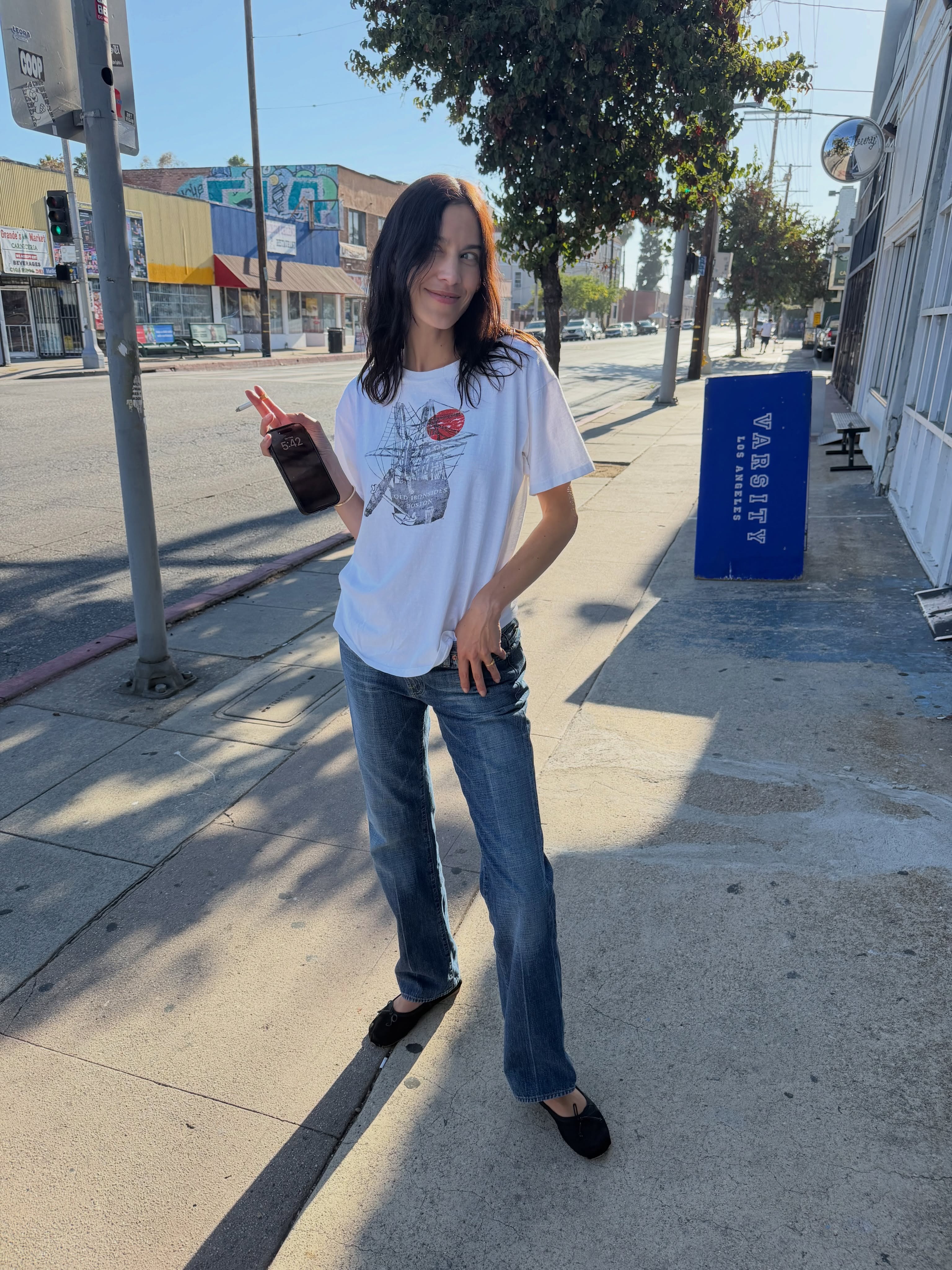 Alexa Chung wears a white graphic tee with skinny jeans and black ballet flats.