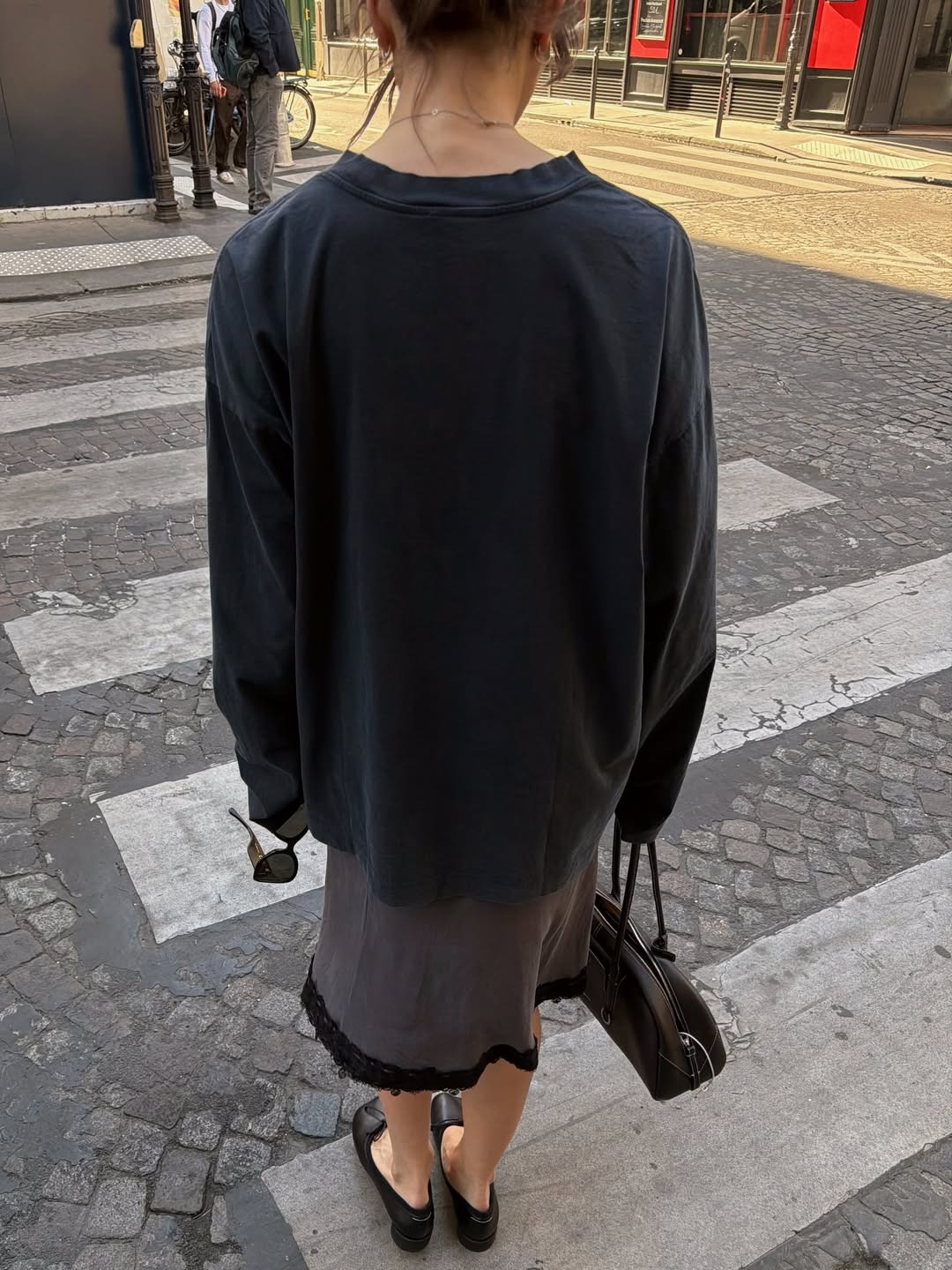 Influencer @poppyalmond wears a baggy long-sleeve t-shirt with a knee-length skirt and heeled ballet pumps.