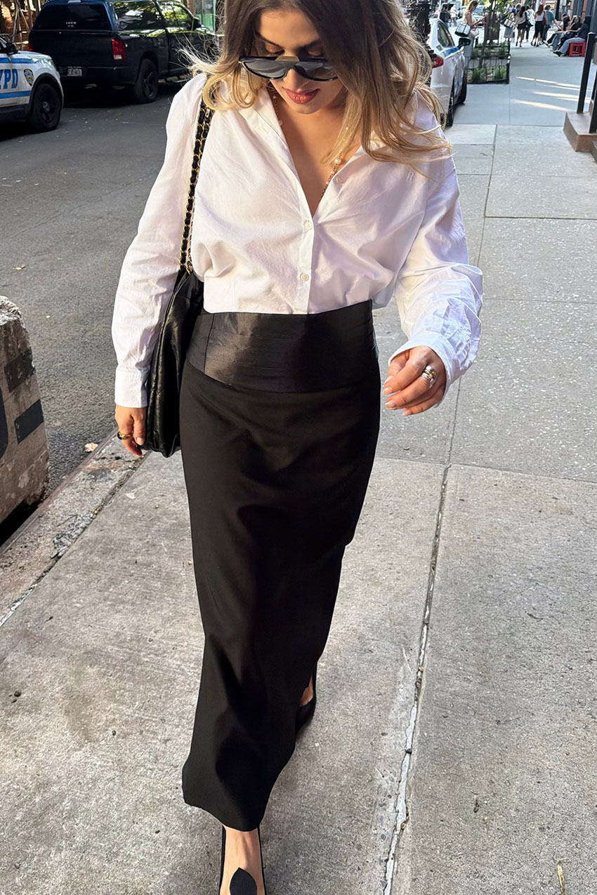 A woman wearing a white button-down, black skirt, and black shoes.
