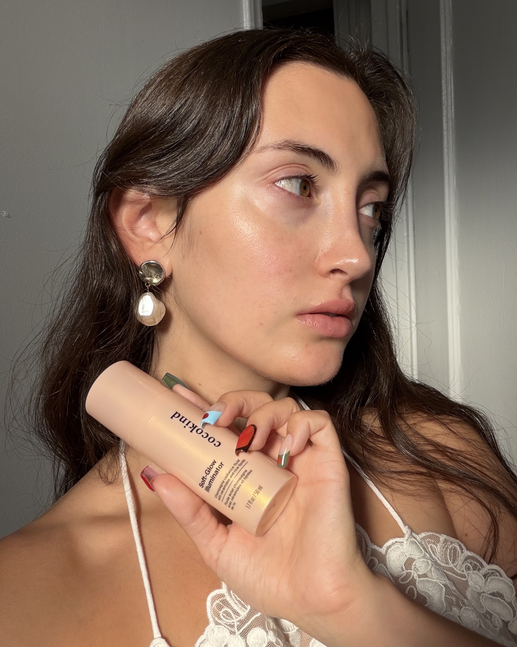An image of WWW associate beauty editor Alyssa Brascia holding and wearing the new Cocokind Soft-Glow Illuminator.