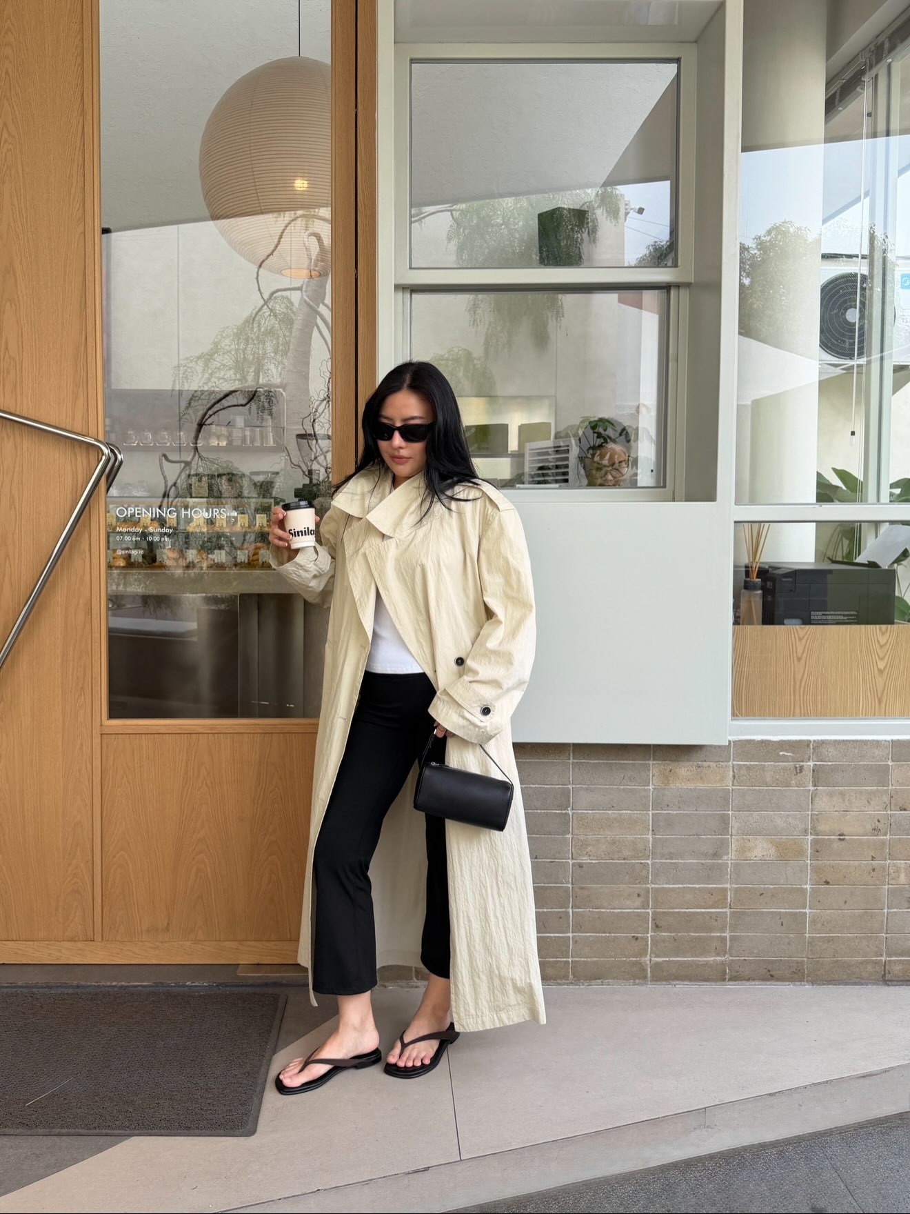 Woman wears light trench coat, white top, black trousers and sandals