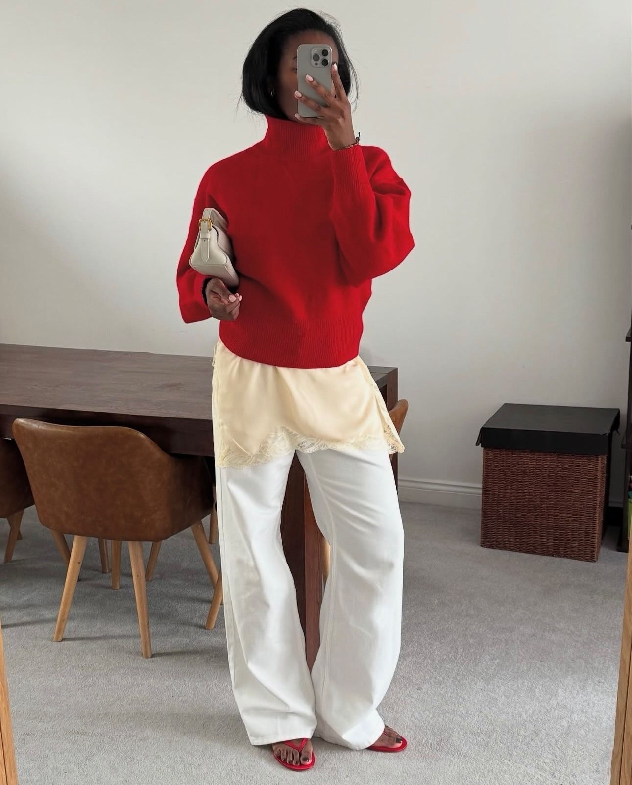 Colourful capsule wardrobe autumn 2026: nlmarilyn. She wears a chilli red jumper and flip flops with a white jeans, a cream lace top and white clutch bag. This image was taken from Instagram.