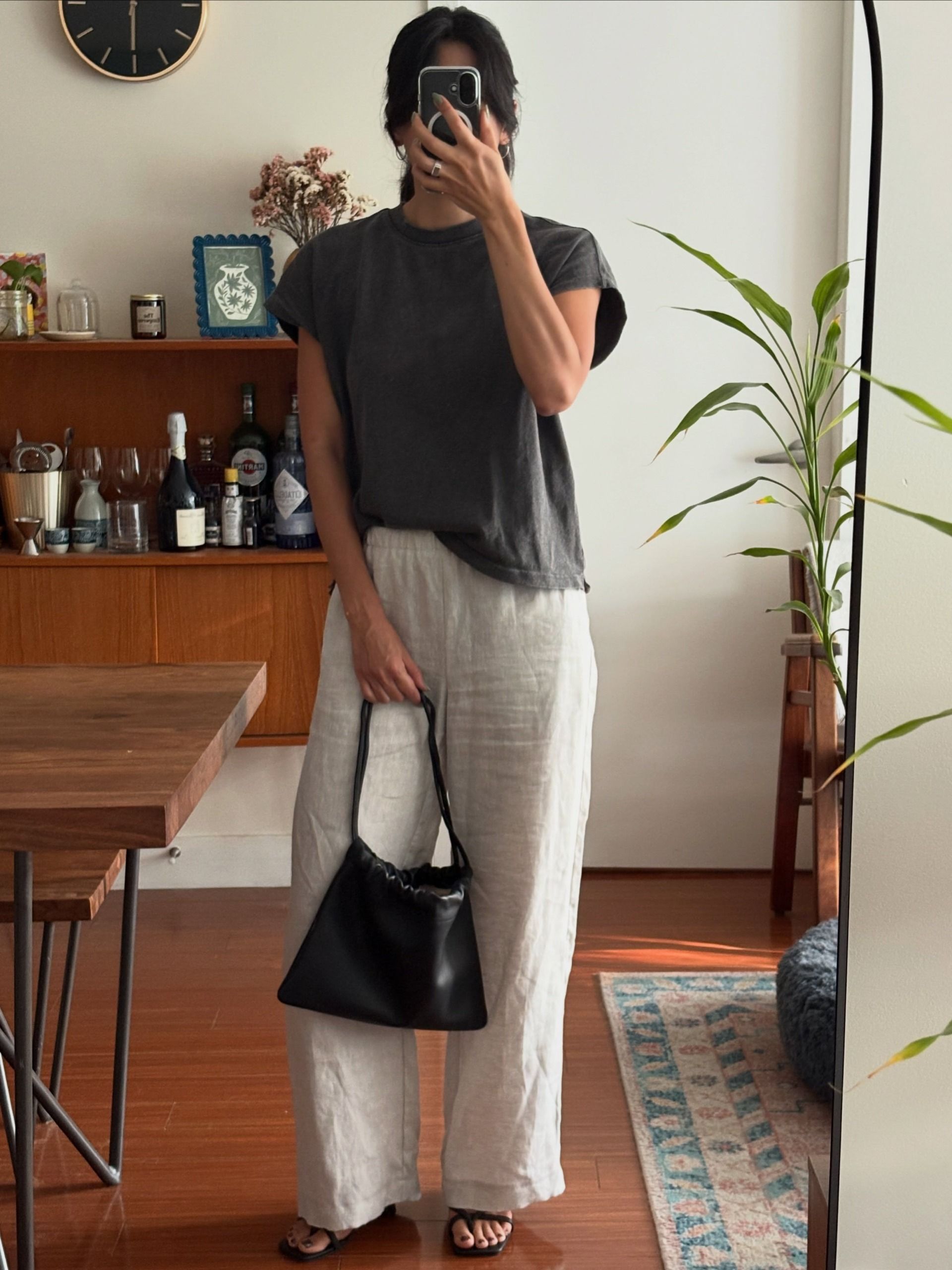 Woman wears grey tee, beige trousers and carries black drawstring bag from The Horse