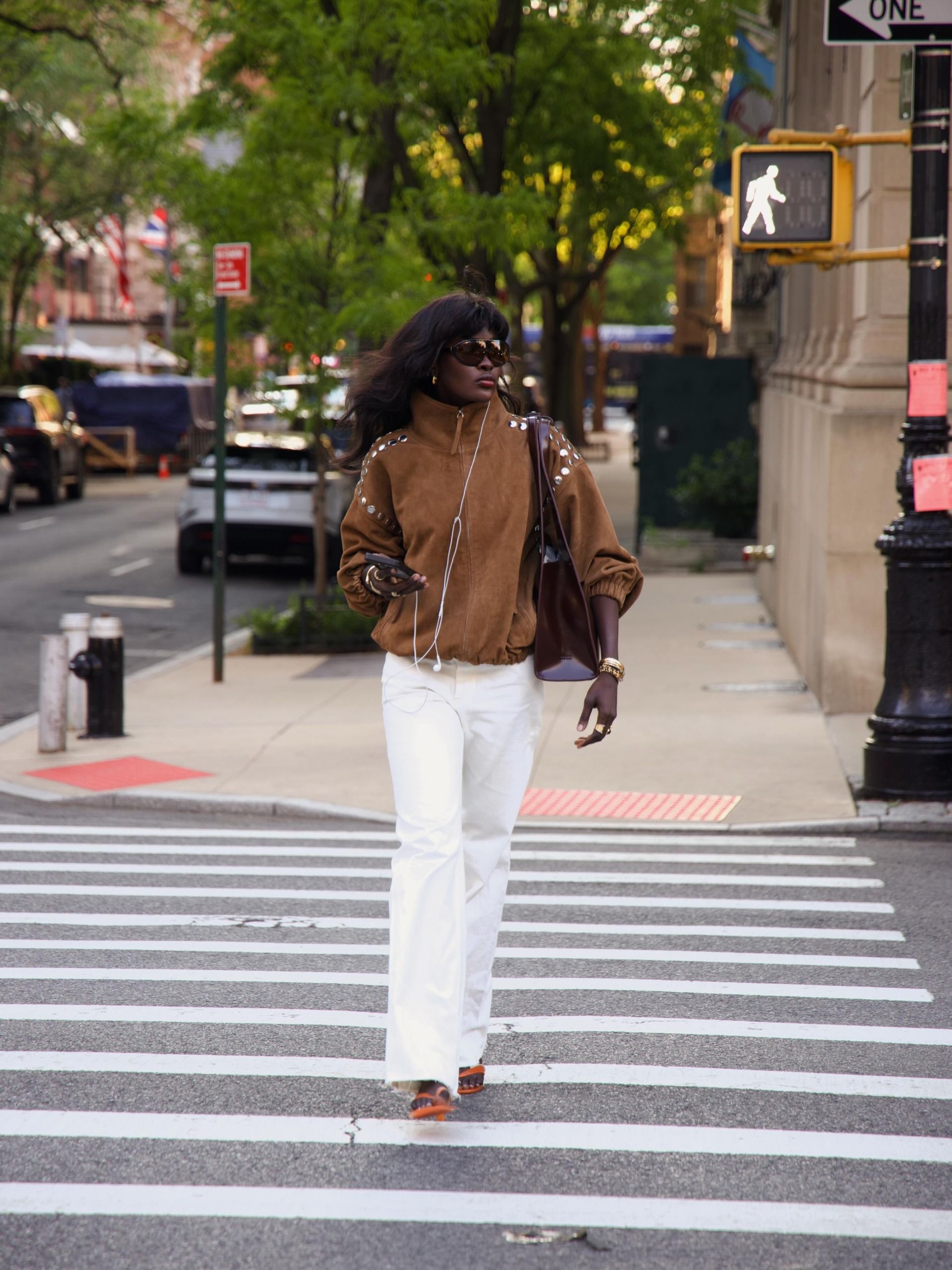 An image of an influencer in New York wearing a suede jacket with white jeans and carrying a leather tote