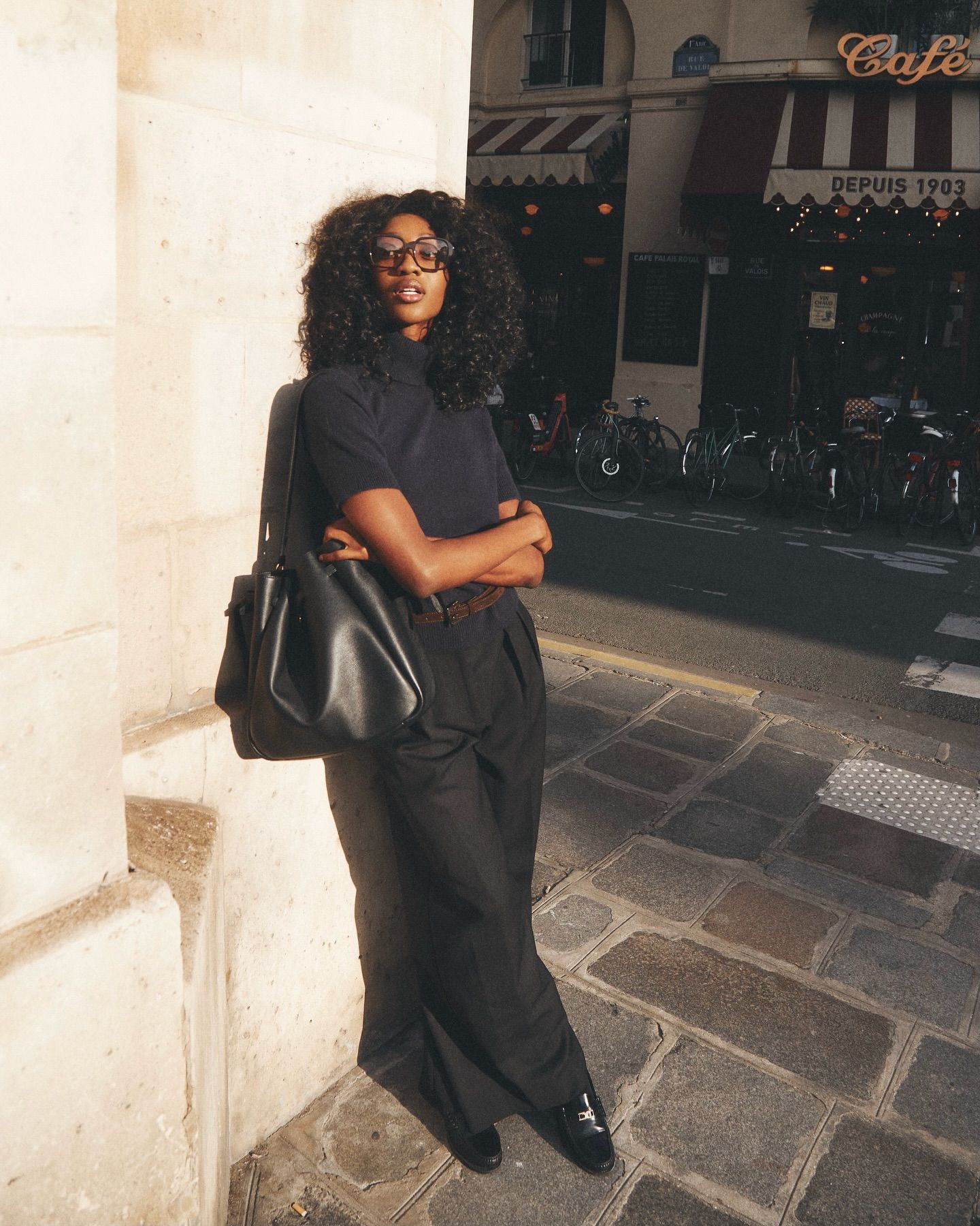 An image of an influencer in Paris wearing a navy short-sleeve, high-neck knit with tailored black trousers and black loafers, carrying a black leather tote