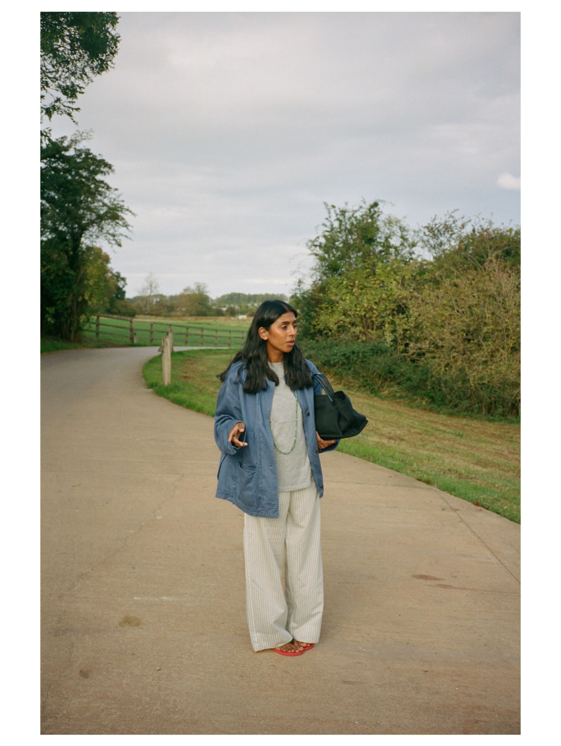 Influencer Monikh wearing a barn jacket, grey t-shirt, striped trousers and red flip-flops.