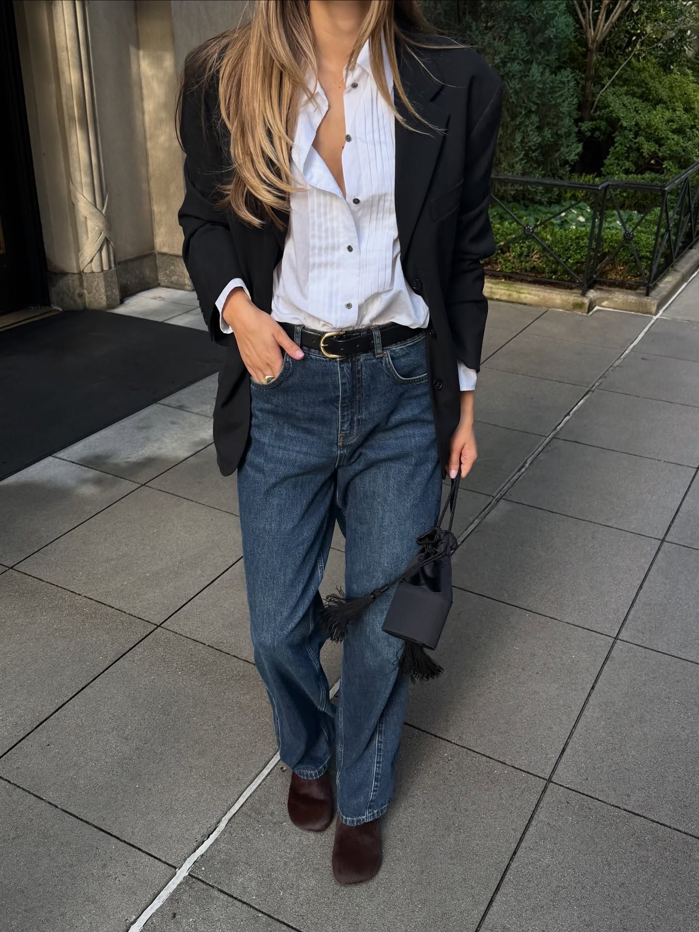 An image of an influencer in New York wearing a white tuxedo shirt under a black blazer with dark-wash jeans and suede brown loafers