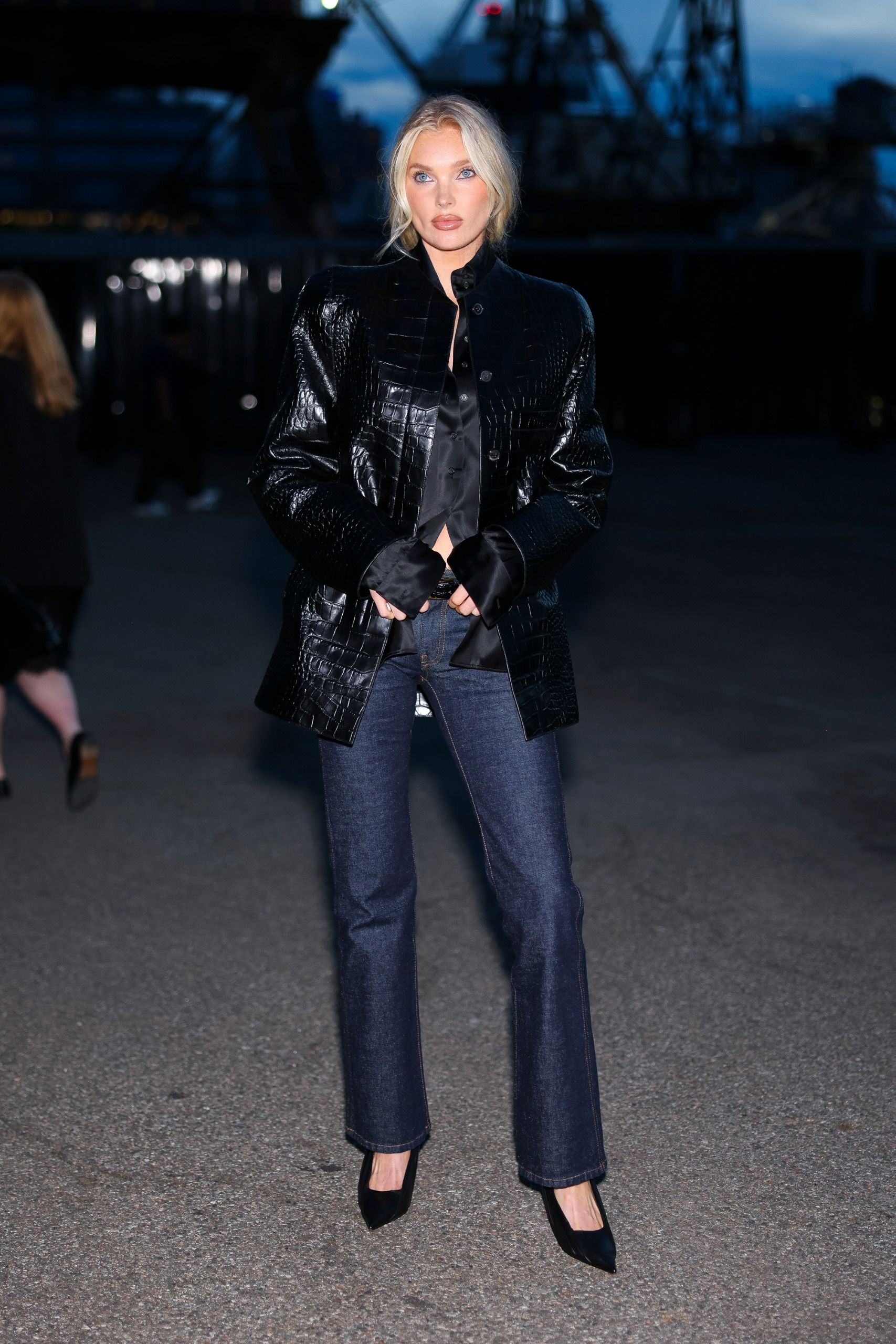 Elsa Hosk wears a black croc-leather jacket, black button-down shirt, low-rise dark-wash jeans, and black pumps.