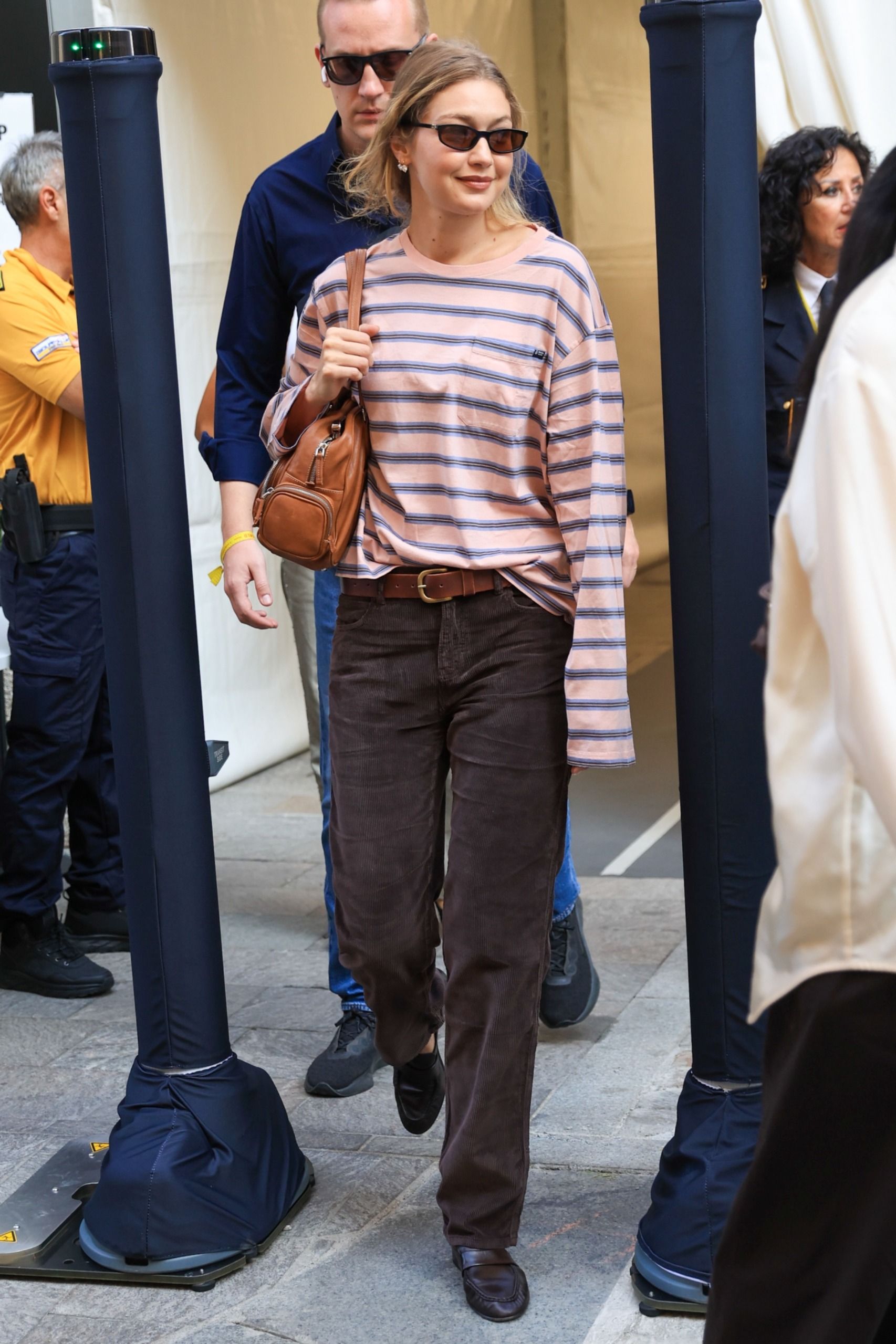 Gigi Hadid walks down the street in Milan wearing brown straight leg jeans with loafers and a striped t-shirt.