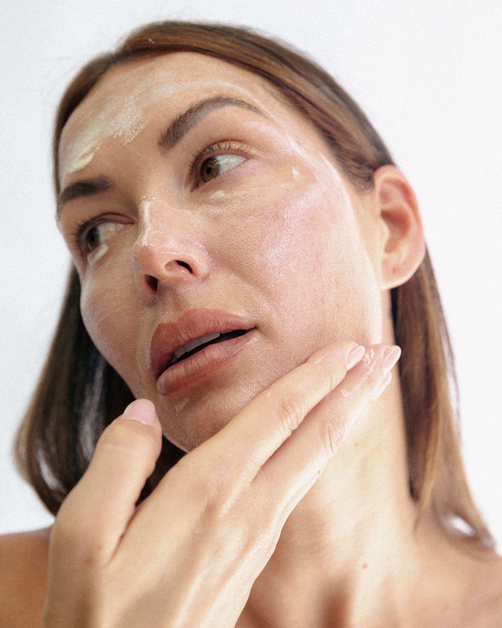 A woman looking to the side as she applies skincare