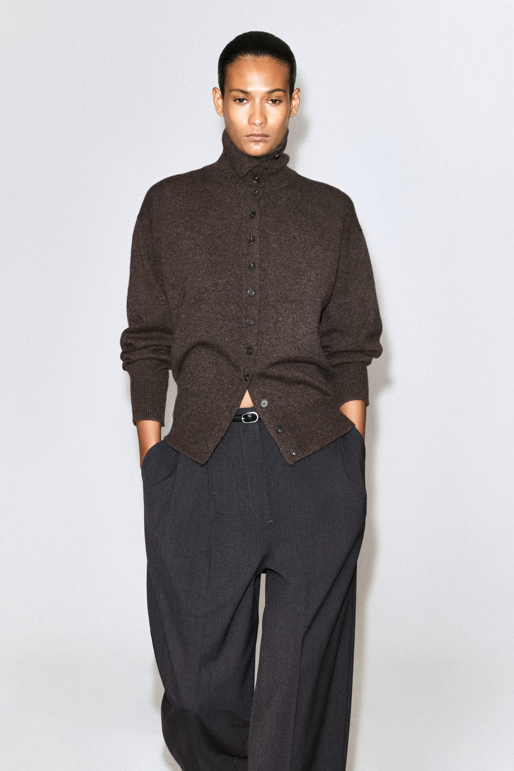 A model wearing a brown Cos turtleneck cardigan and black trousers.