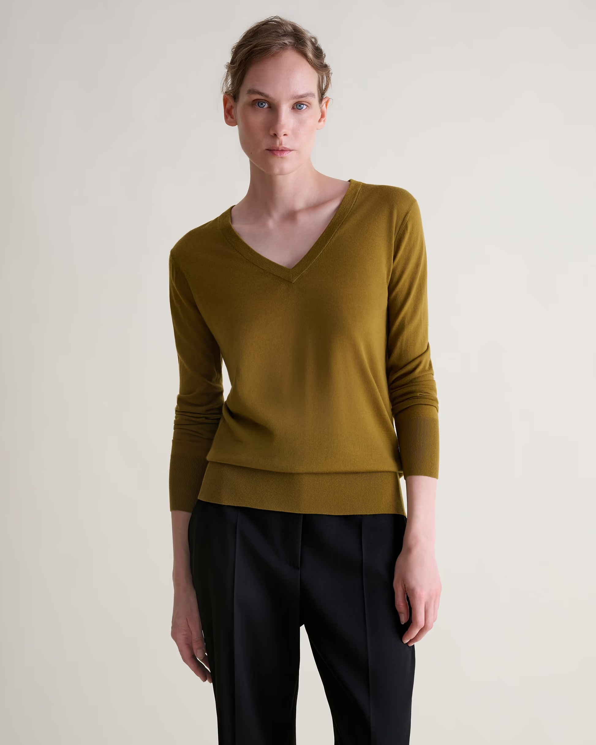 A model wearing a green Rise & Fall v-neck jumper.