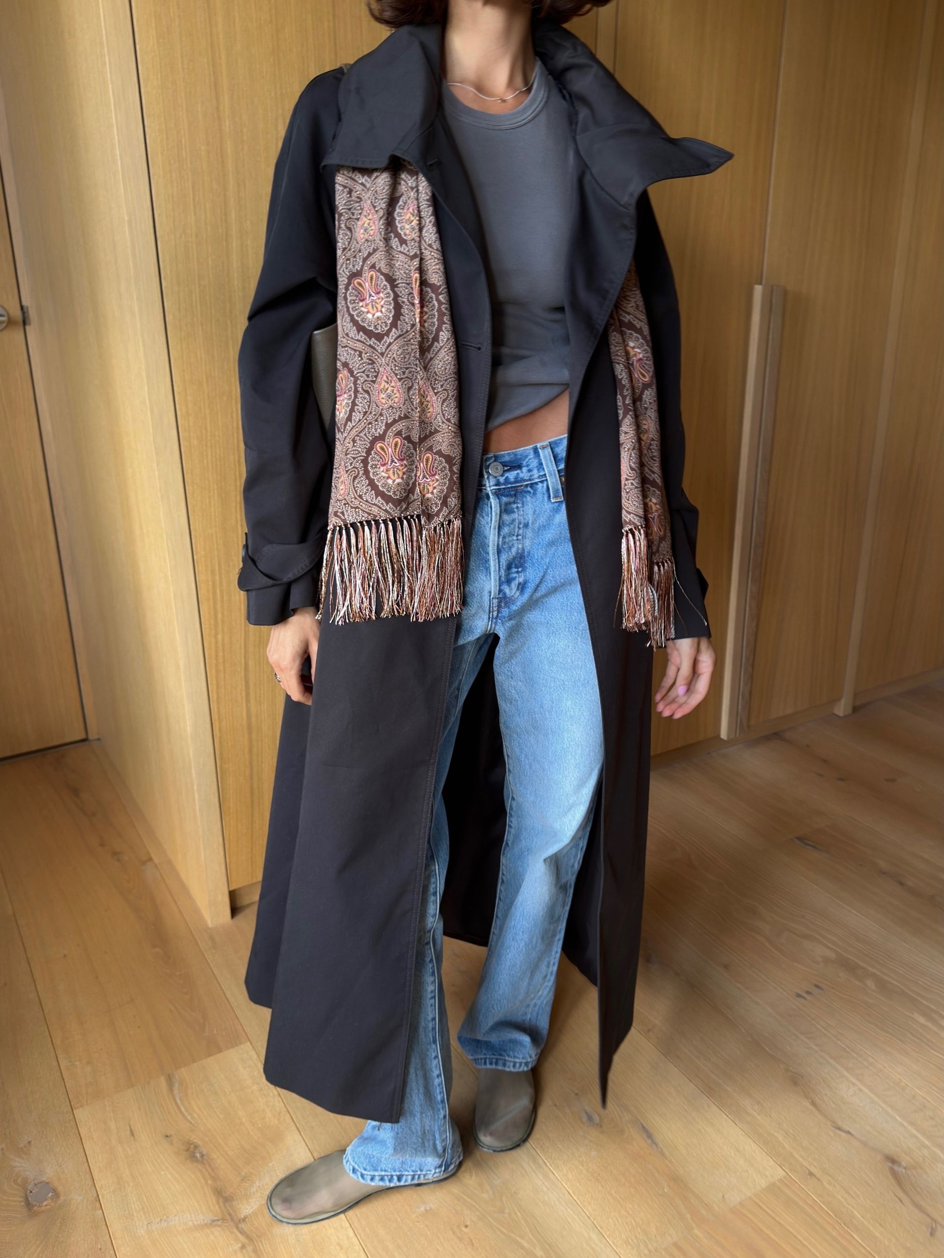 fashion influencer wearing a black trench, jeans, and paisley scarf