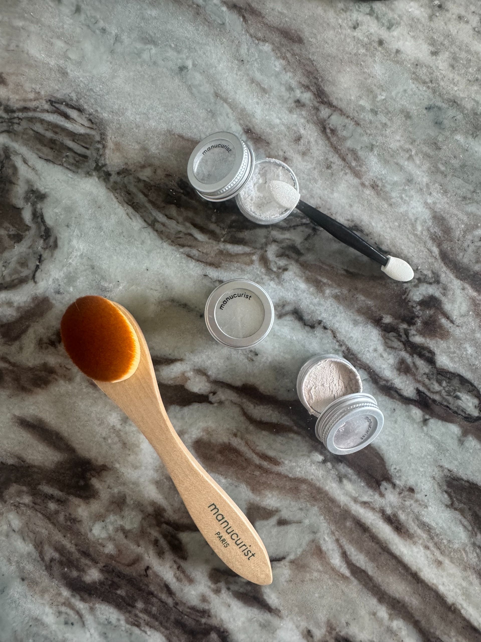 The Manucurist Glazed Powders and brush on a marble table