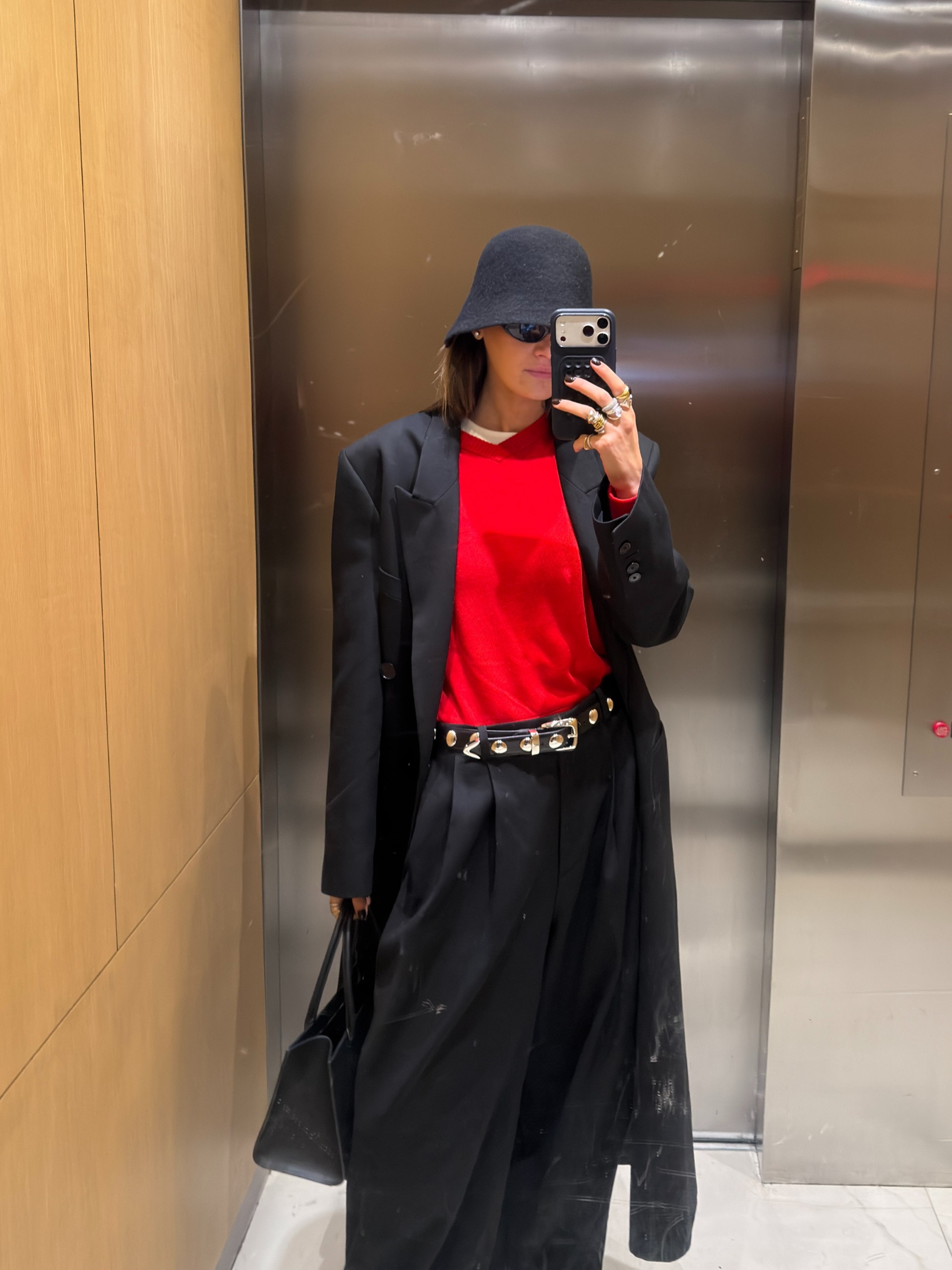 Influencer Coco Schiffer wearing a red jumper with black trousers, studded belt and black coat.