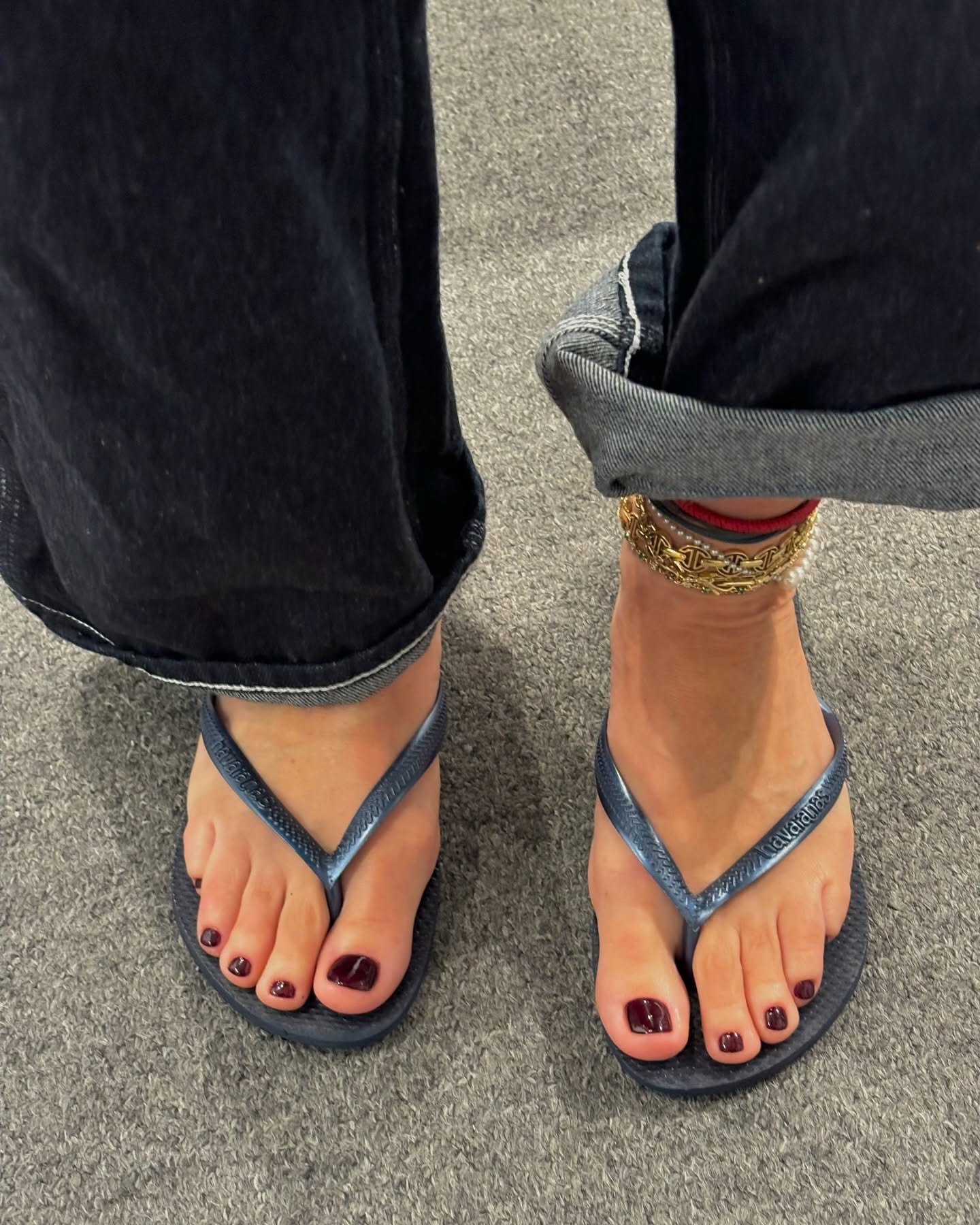 A woman wearing navy jeans and flip flops with a burgundy pedicure