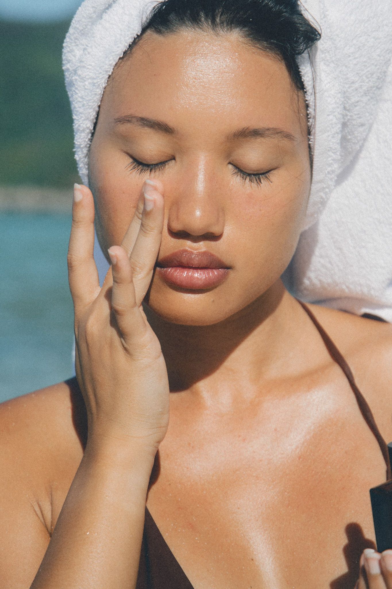 A woman wearing a towel in her hair, closing her eyes as she touches her under eye