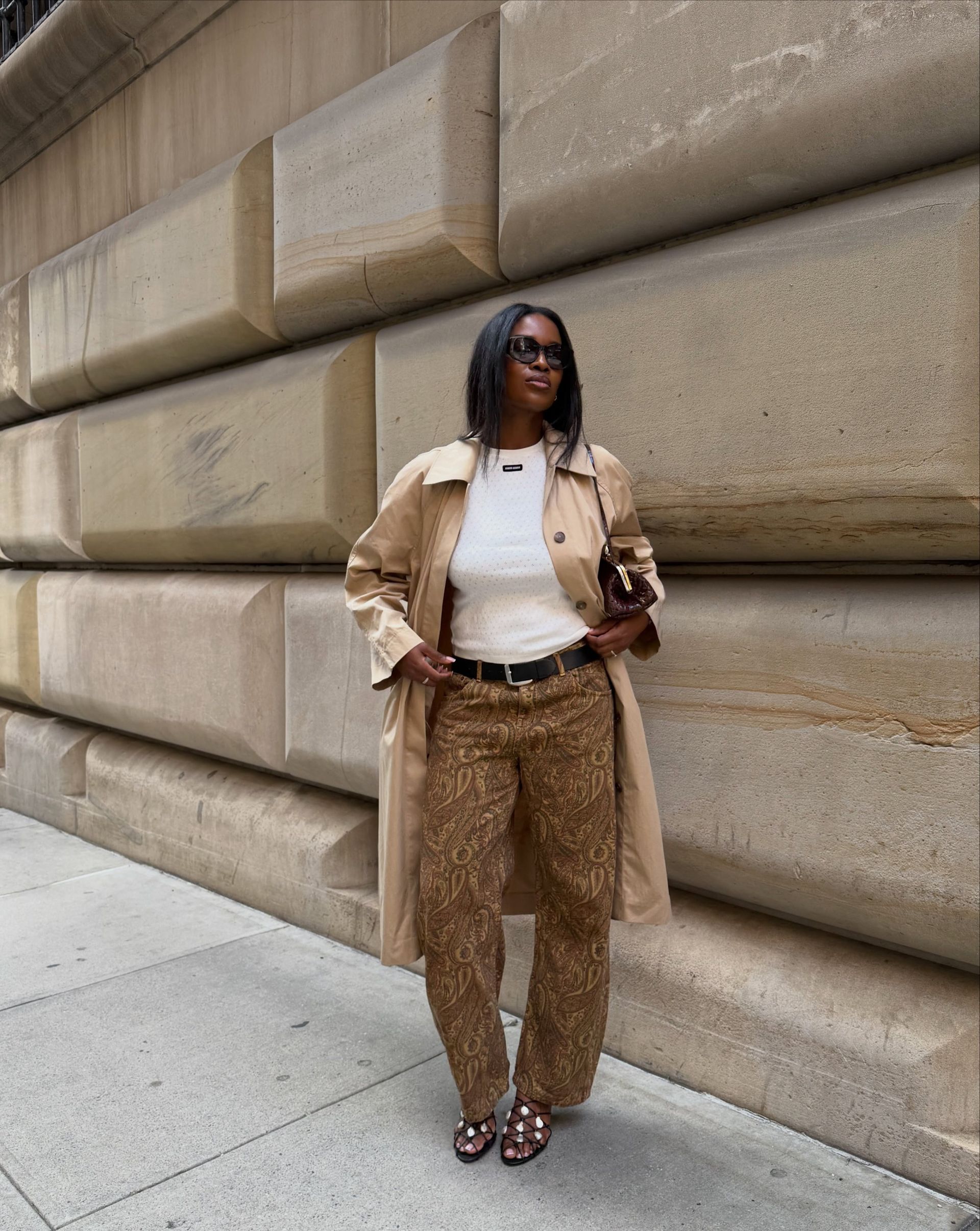 An image of an influencer in New York wearing a white T-shirt, a beige trench and dark beige jeans with a paisley pattern on them