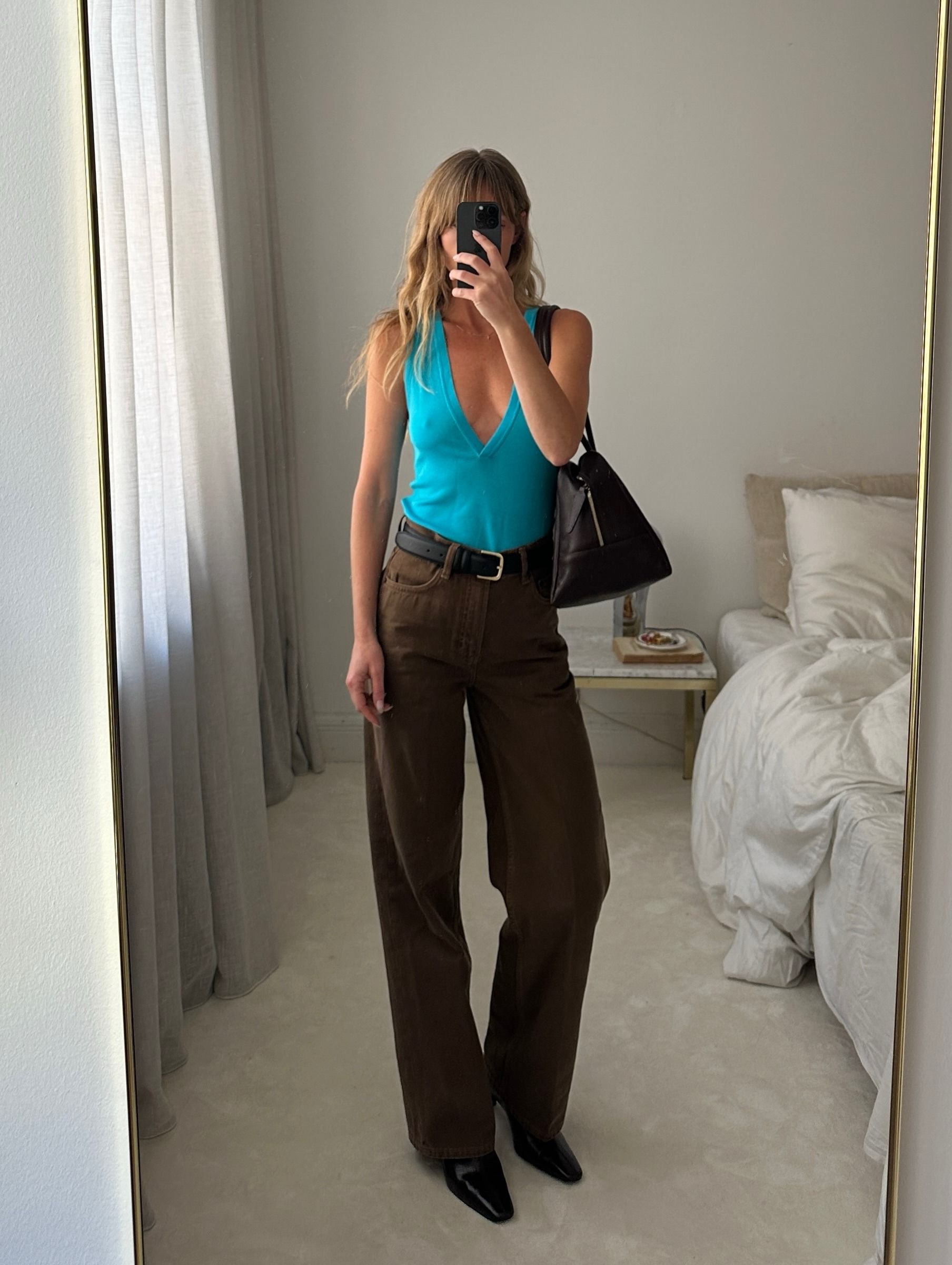 Colourful capsule wardrobe autumn 2026: _jeanettemadsen_ wears an aqua top. She styles it with brown trousers, black boots, a black belt and a black bag. This image was taken from Instagram recently.