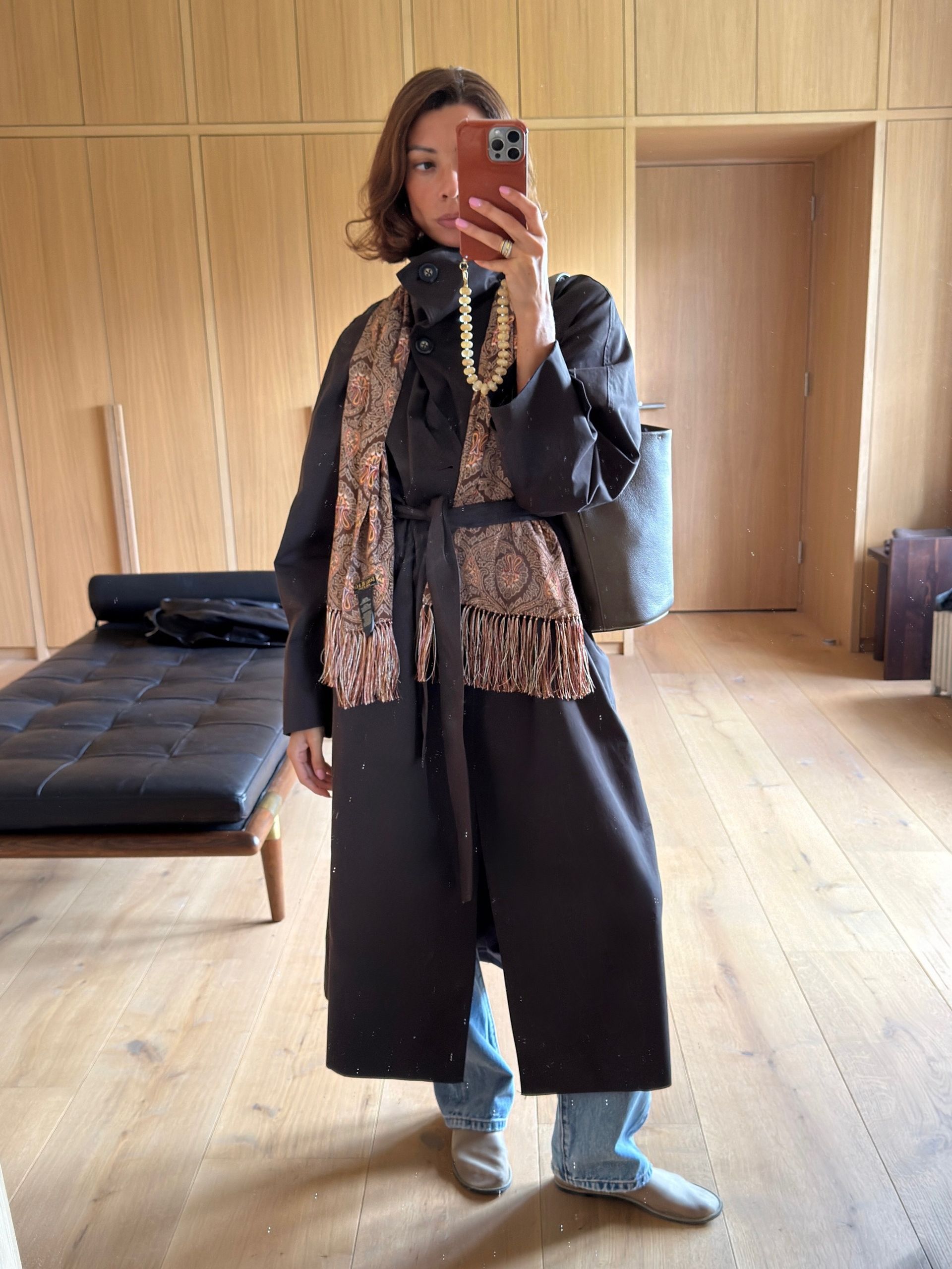 Influencer wearing a black trench with jeans and a fringed paisley scarf