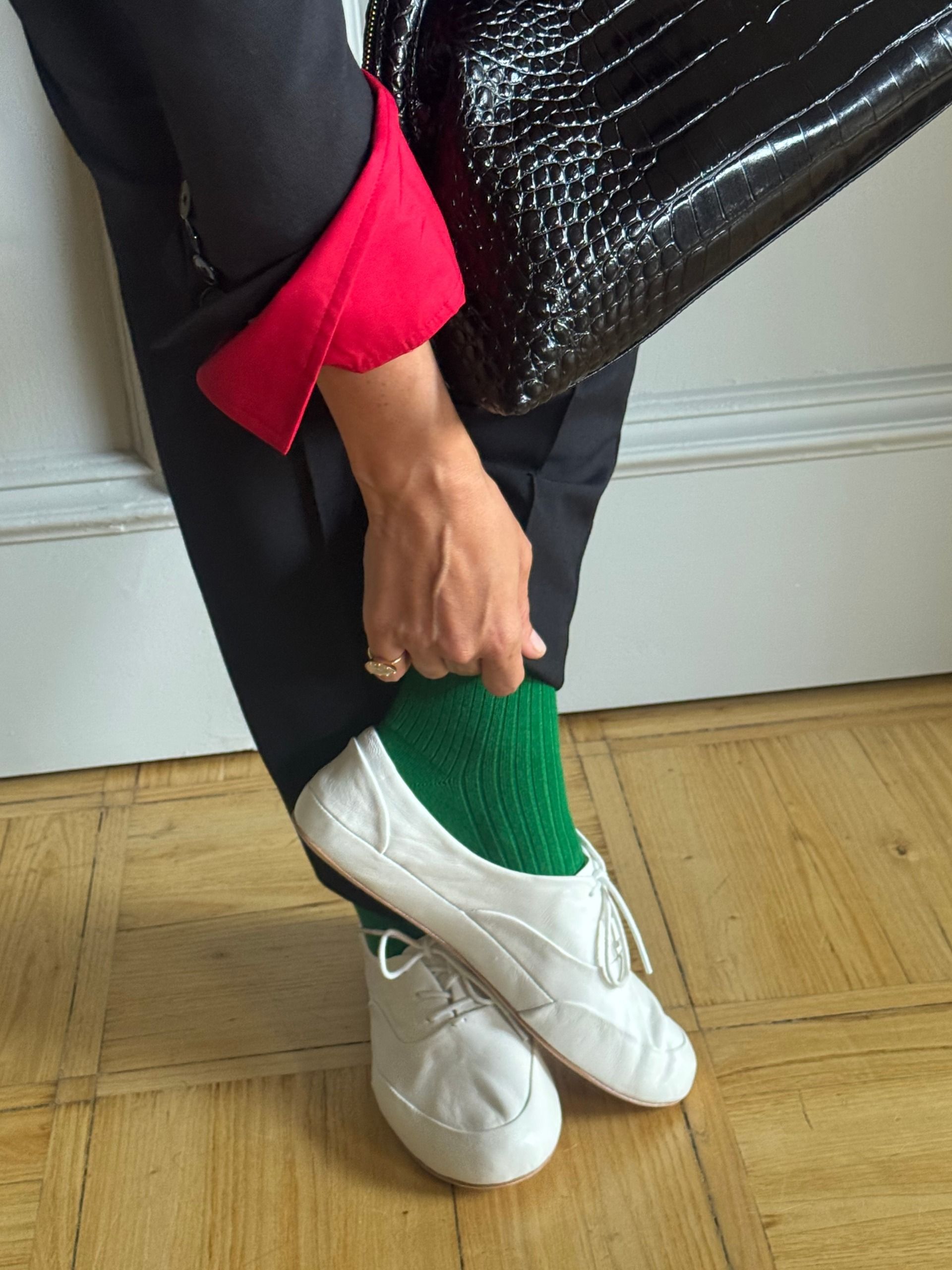Blanca Miro wears a black suit, red shirt, green socks and white trainers with a croc bag