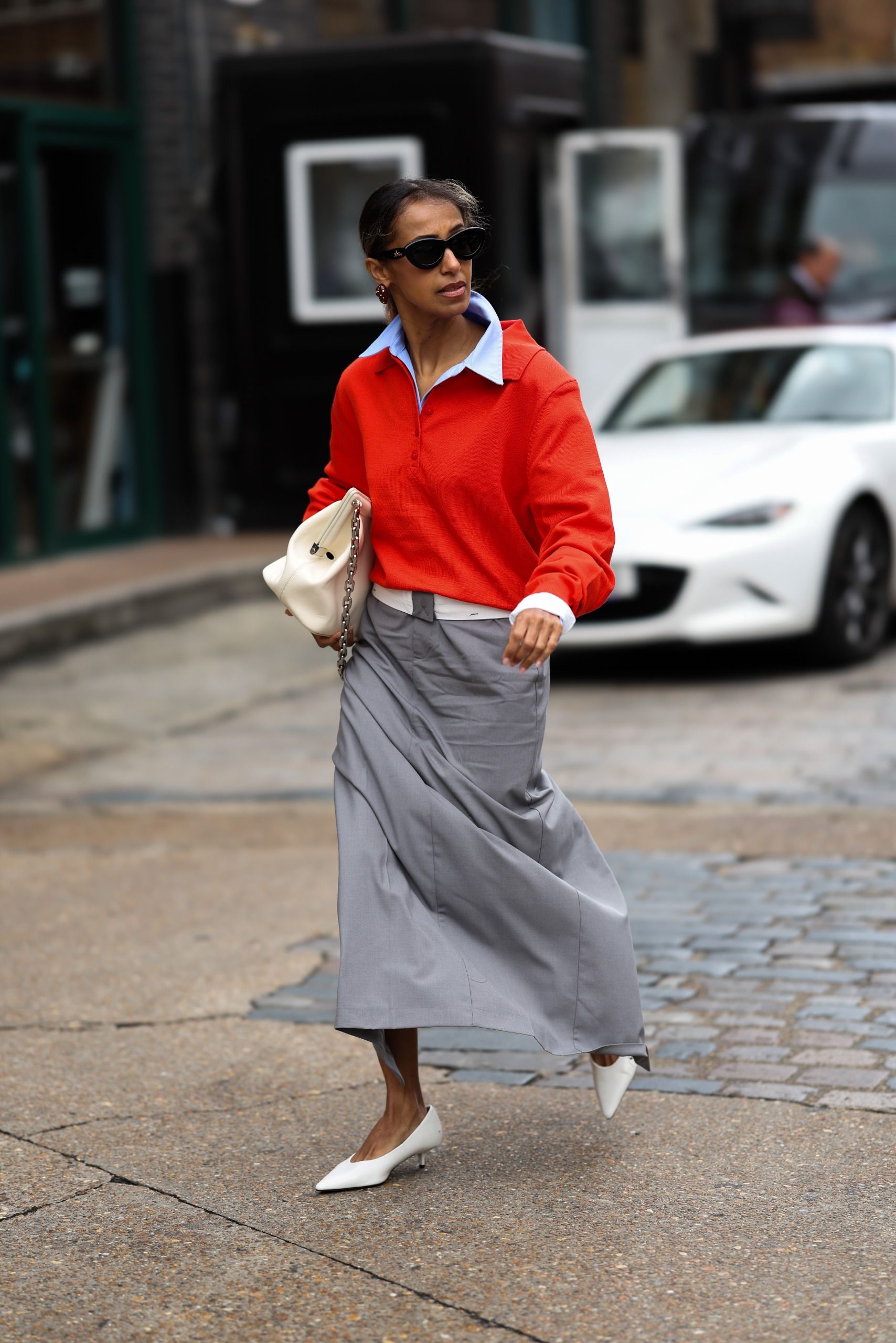 A woman in London wears a polo sweater with a maxi skirt and pumps.