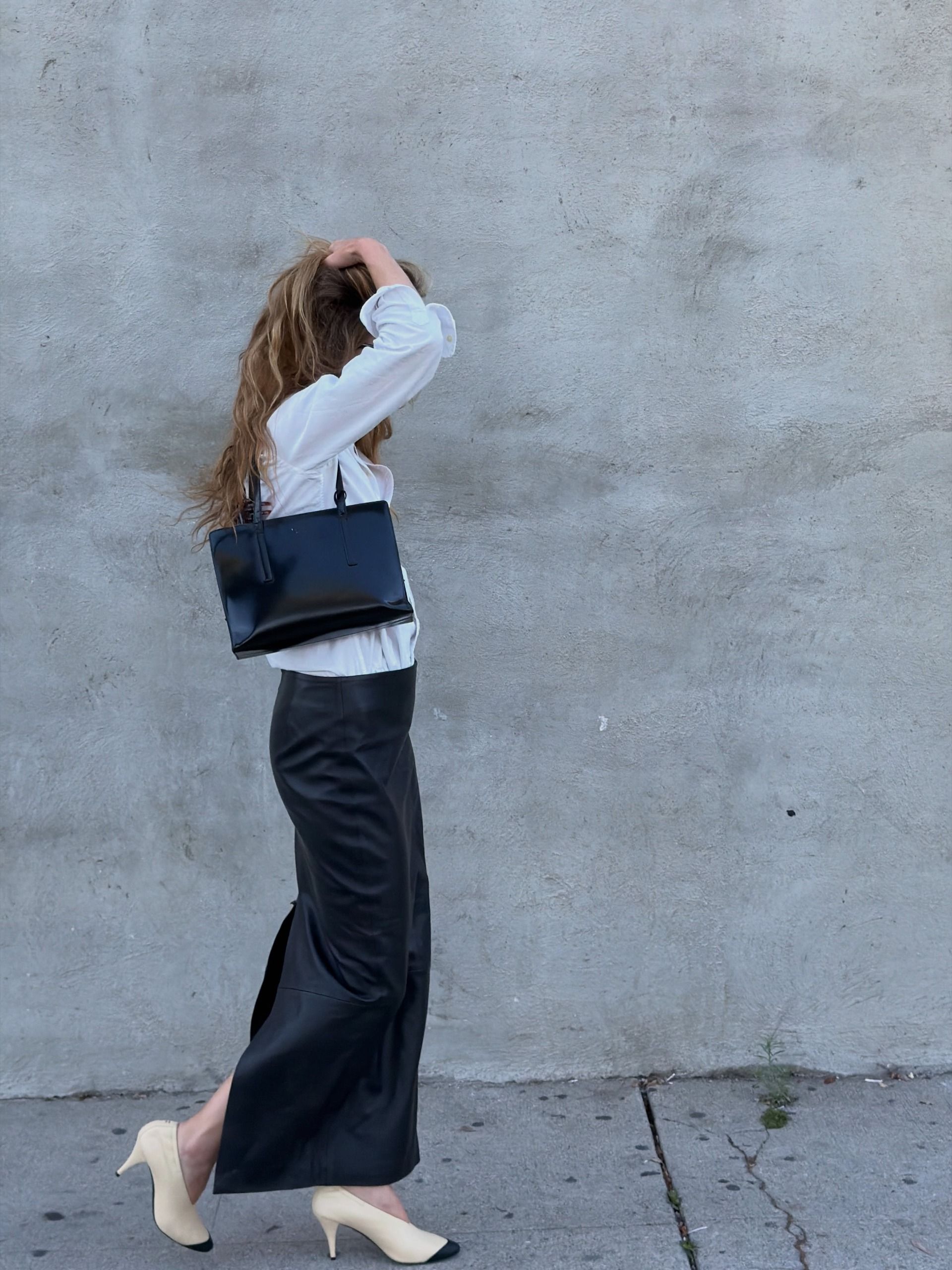 Eliza wears cap-toe heels, a black satin skirt, and a black bag.