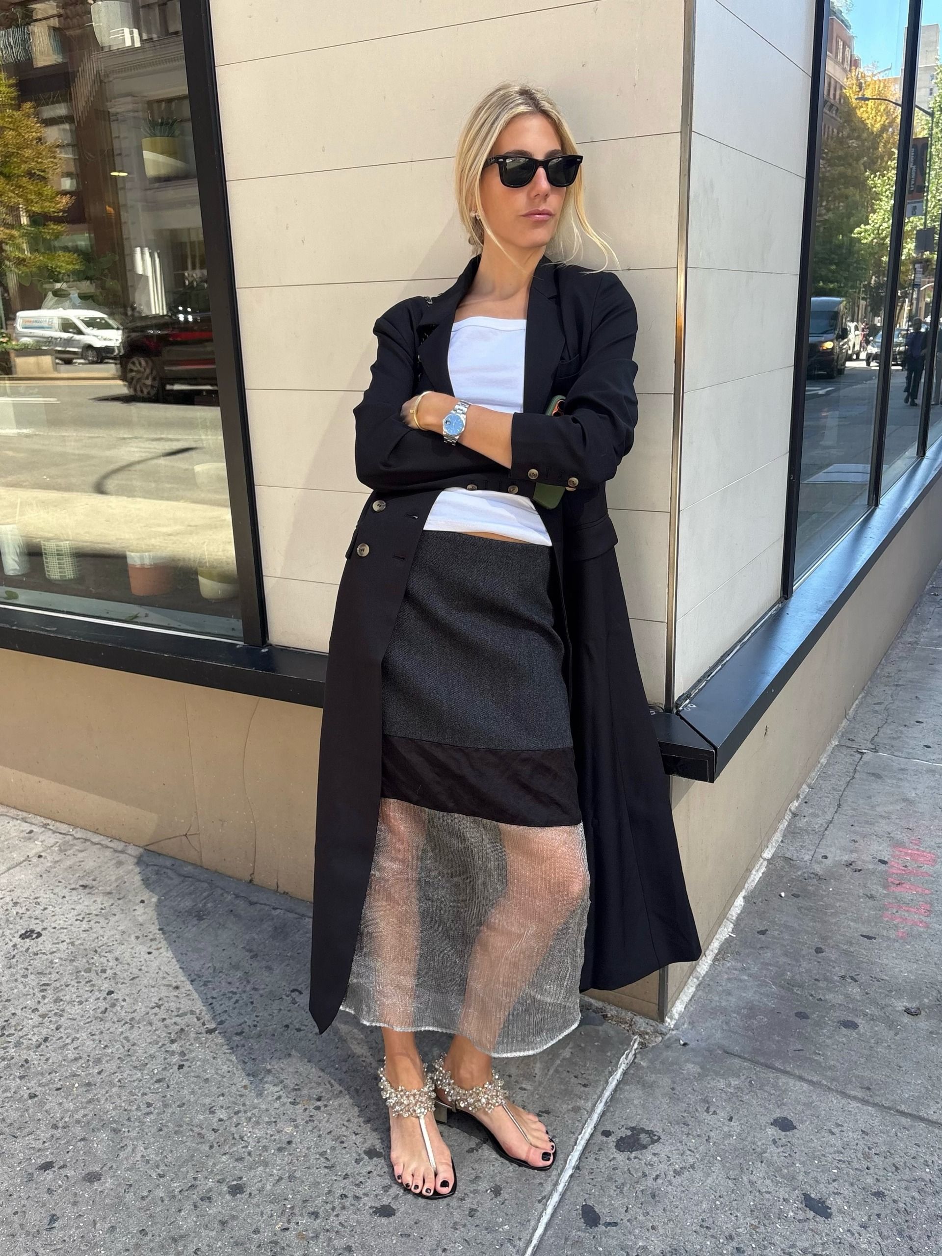 An image of an influencer in New York City wearing a sheer skirt with a long black coat and white top.