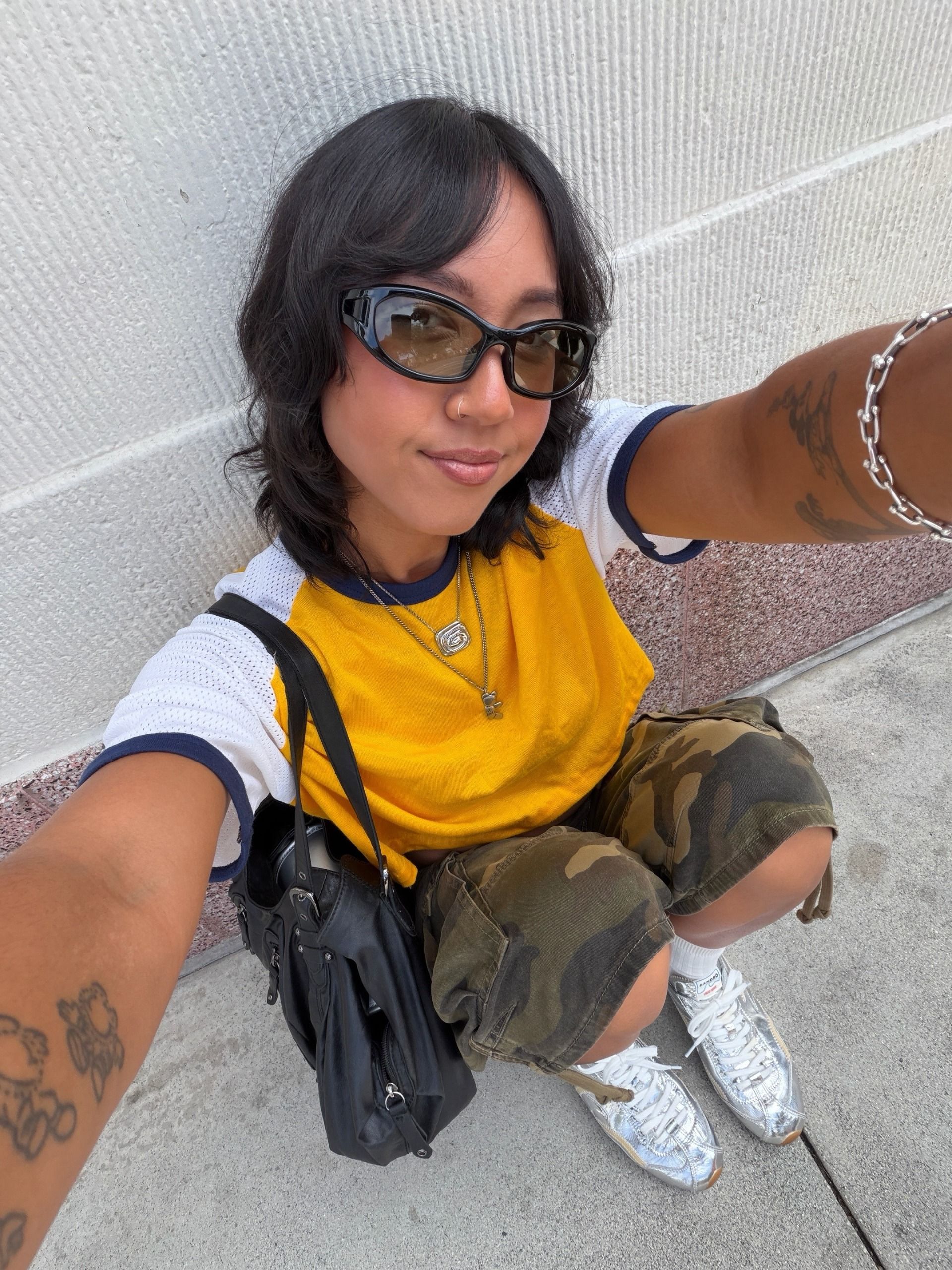 @shhtephs wearing a Baseball tee, camo shorts, and silver sneakers