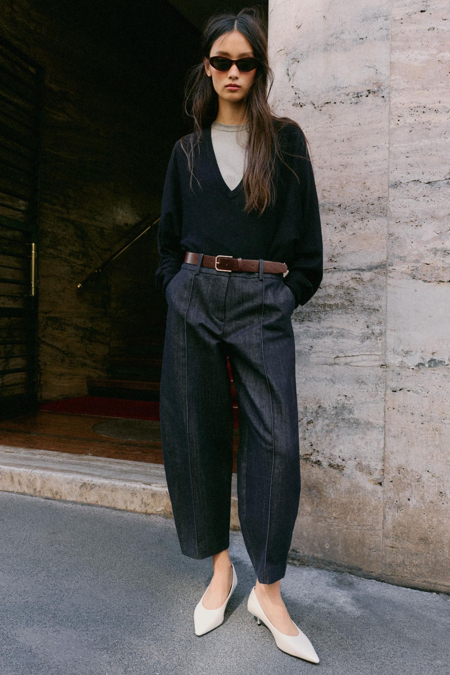 Model wears barrel leg jeans, black sweater, and white kitten heels.