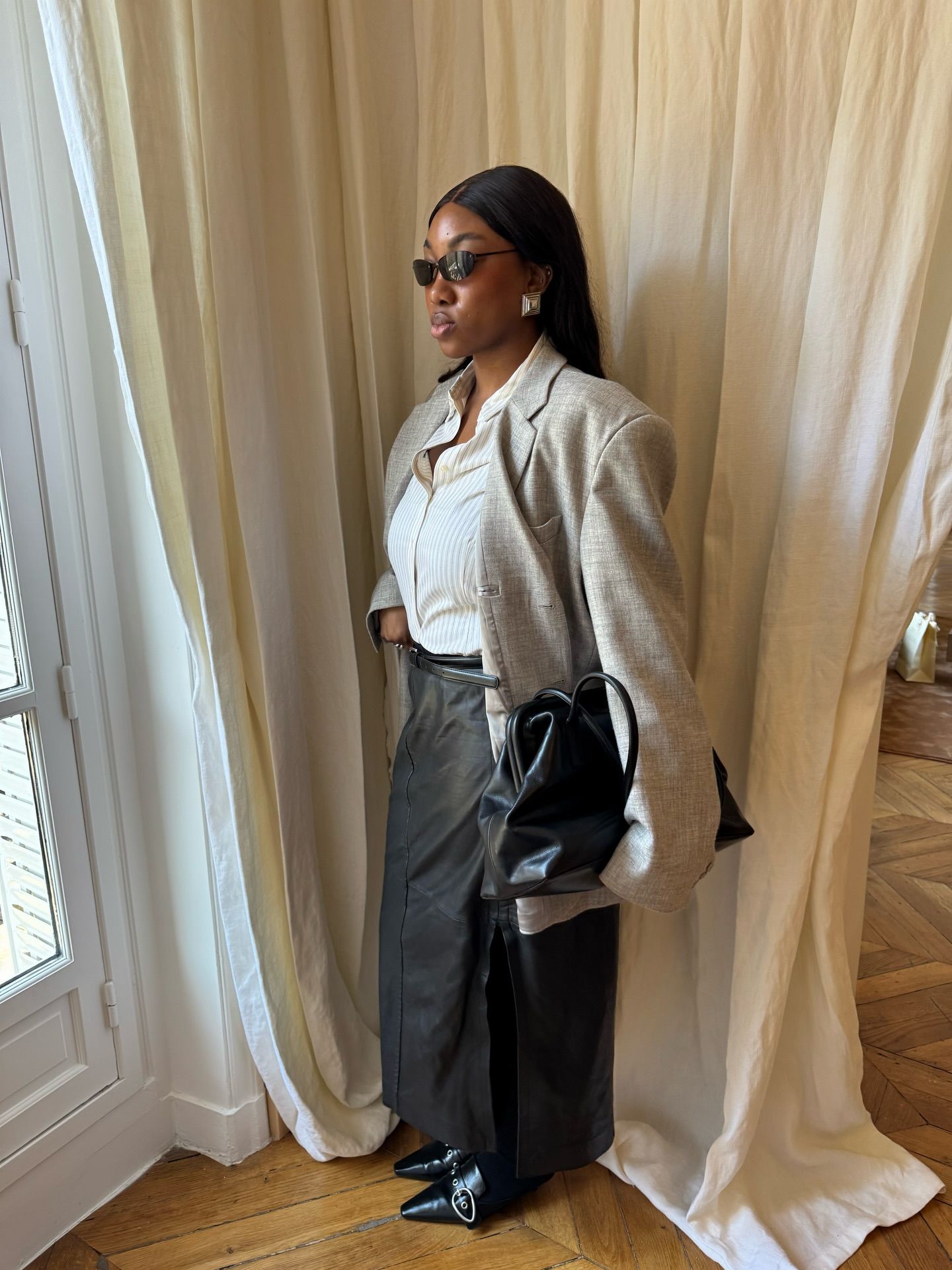 An image of an influencer wearing a beige blazer over a white button-down with a black leather skirt and trendy black heels that are not a dated autumn shoe trend