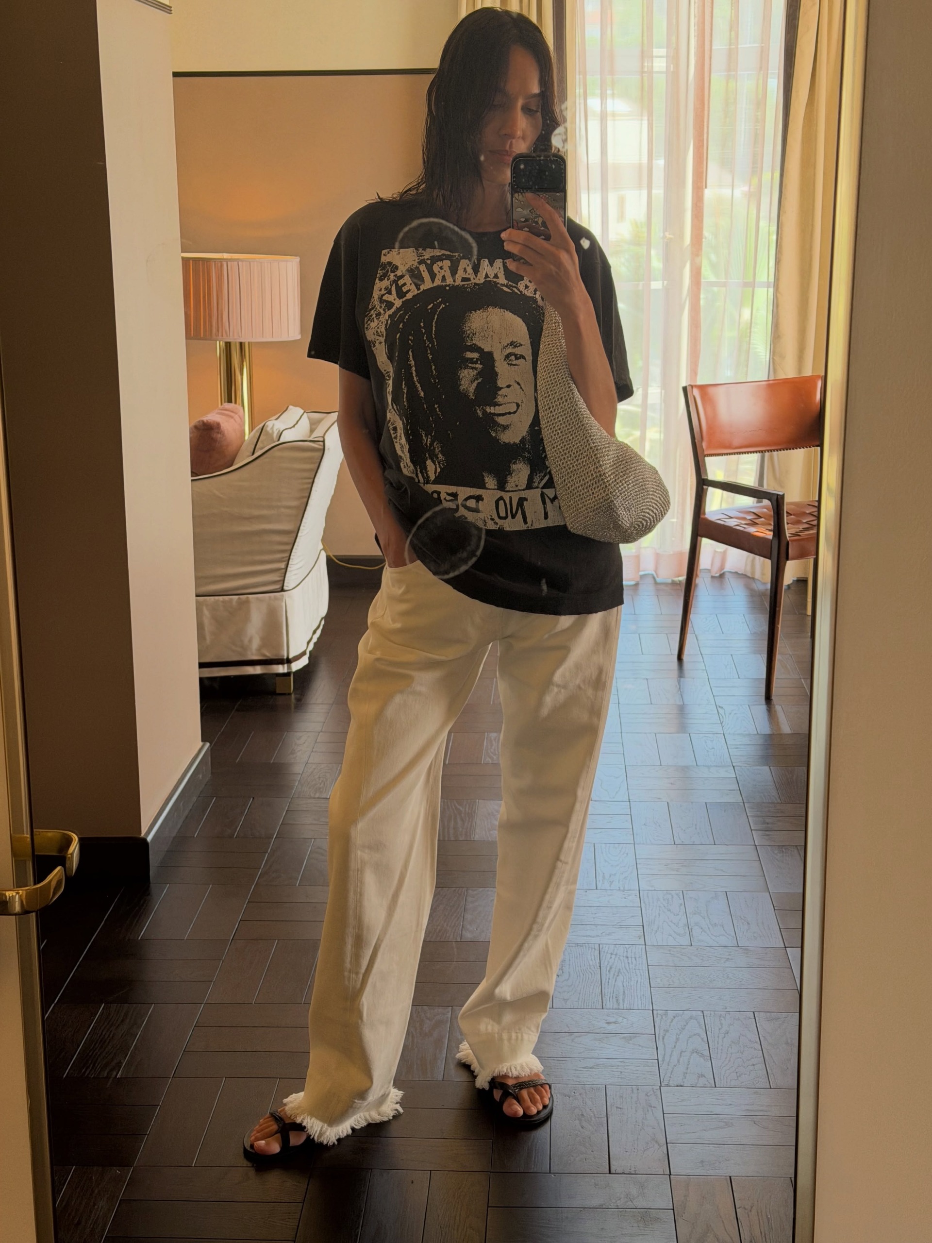 Alexa Chung takes a mirror selfie wearing white frayed jeans with an oversized shirt and t-shirt.