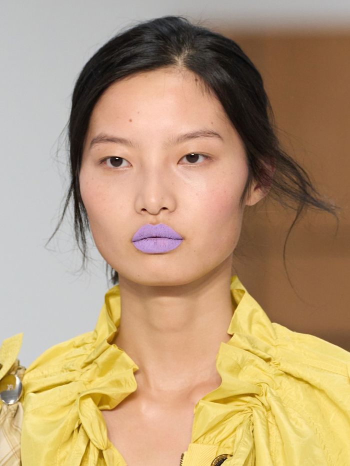 A model walking the runway at the S/S 27 Burberry show with purple lipstick