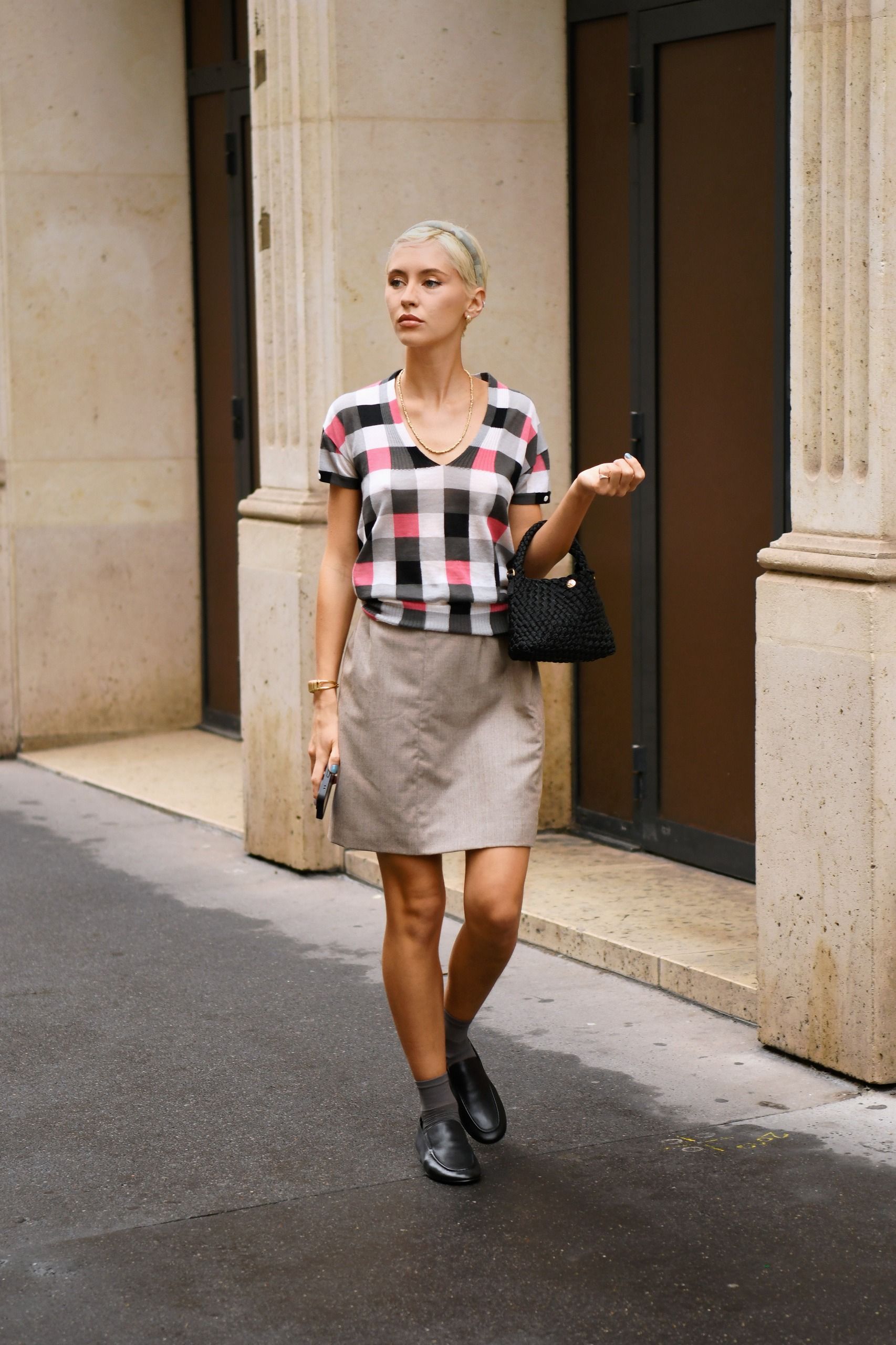 Iris Law steps outside in Paris wearing black Dune loafers with a grey miniskirt and a v-neck t-shirt.