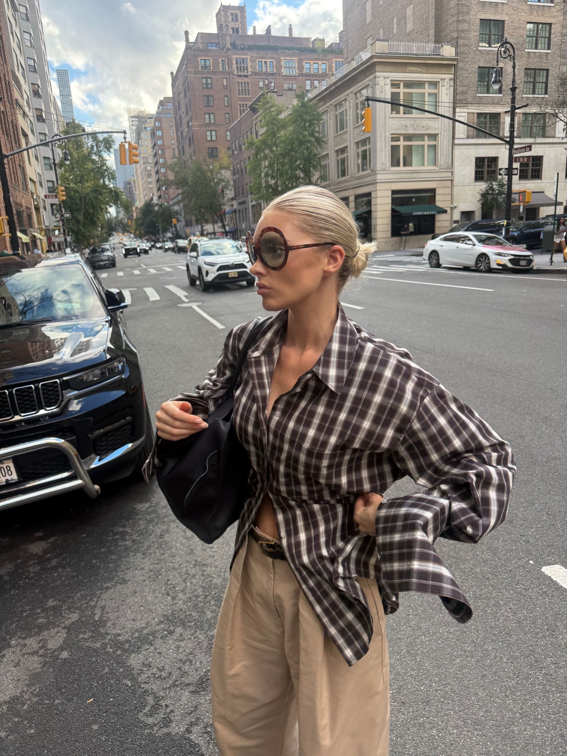 An image of an influencer wearing a plaid button-down shirt in brown and white colours with beige balloon trousers and bug-eye sunglasses