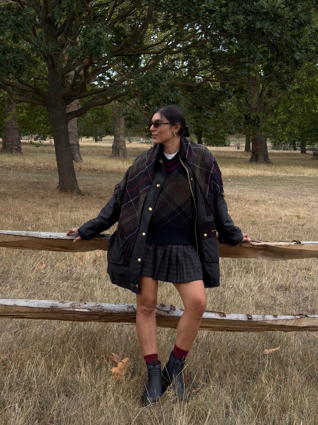 India Cardona wears a navy checked jacket with a pleated miniskirt whilst reclining on a wooden fence