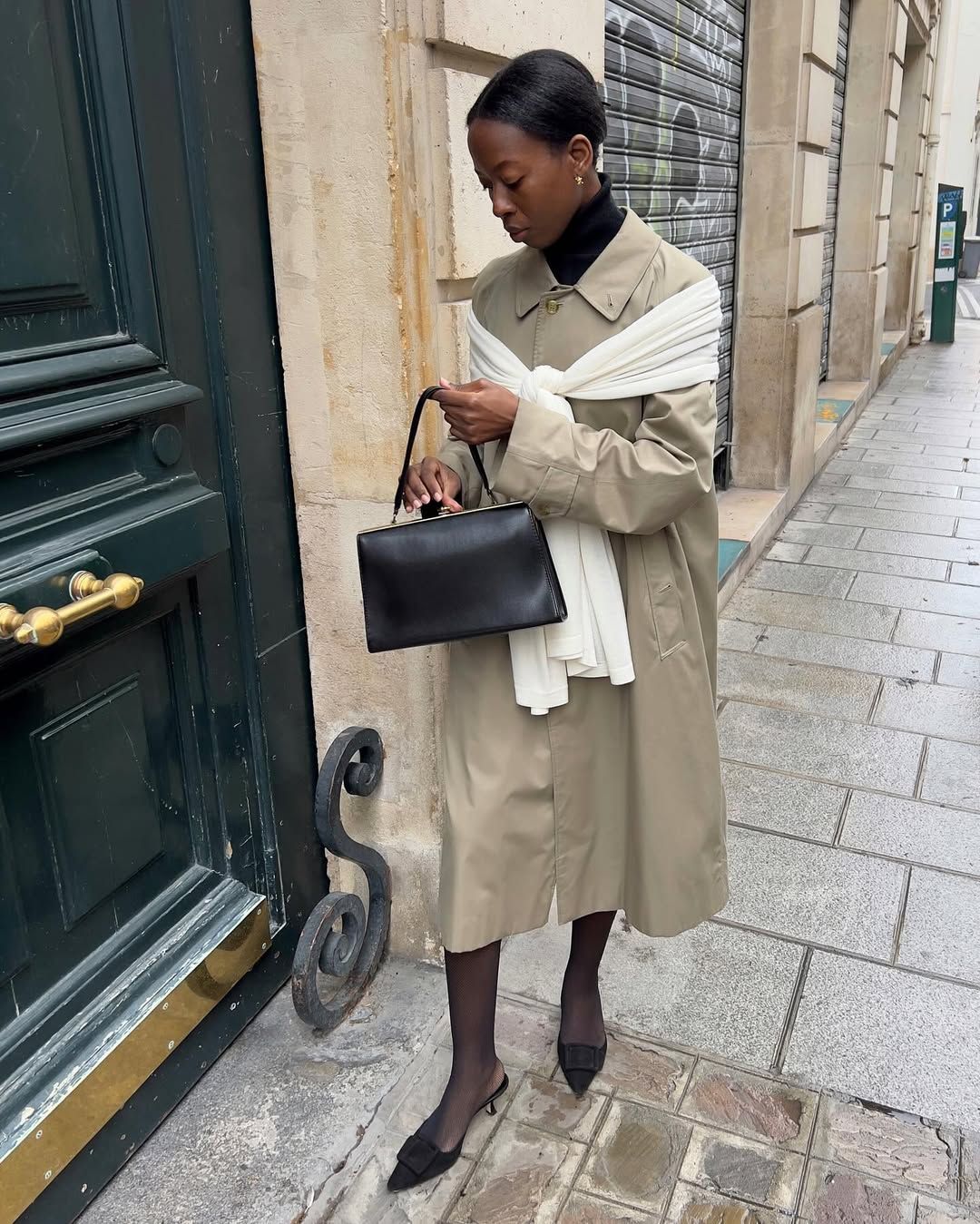 An image of @sylviemus_  wearing a trench coat with heeled mules and tights.