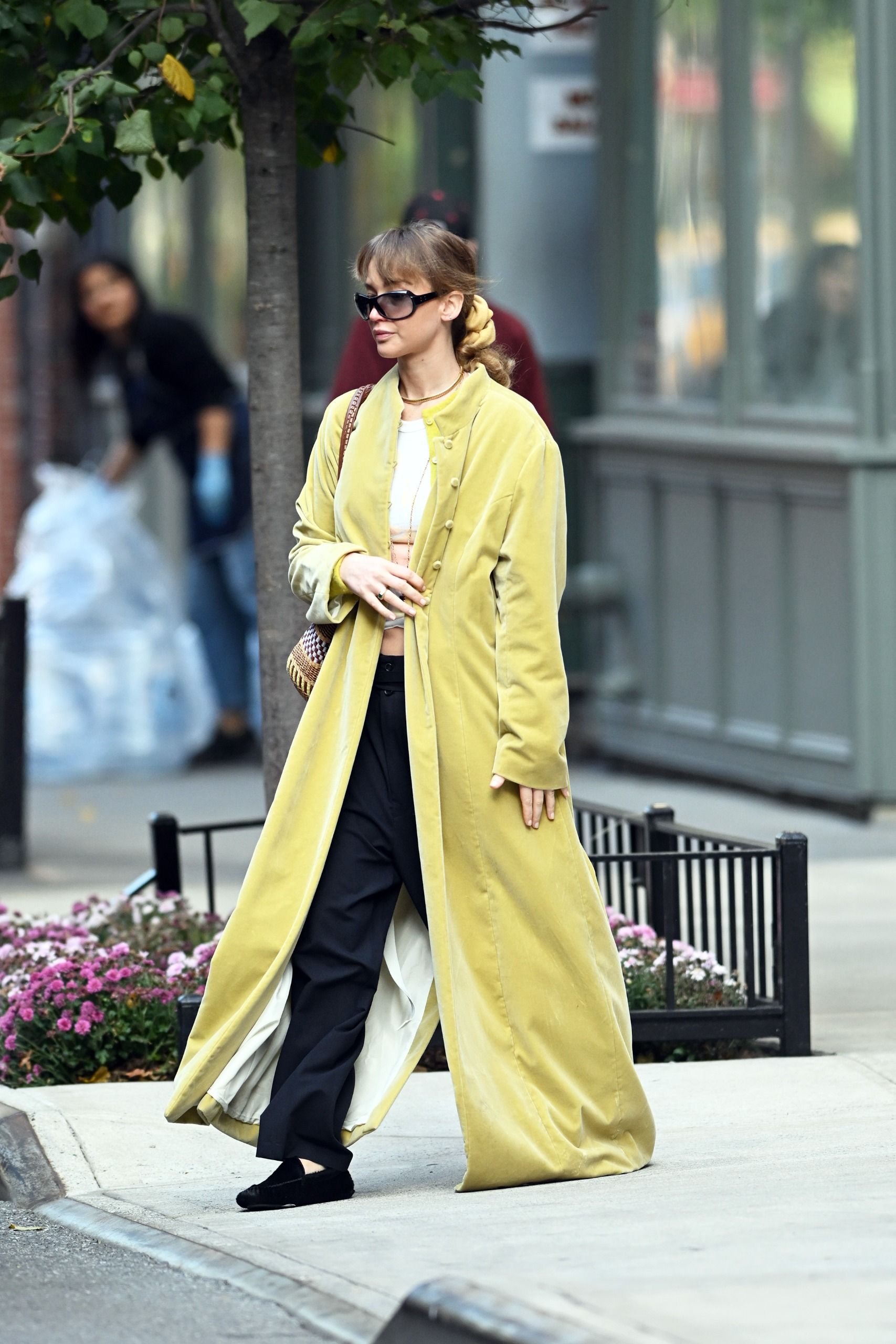 Jennifer Lawrence walks down the street wearing a house coat with a white t-shirt and black trousers.