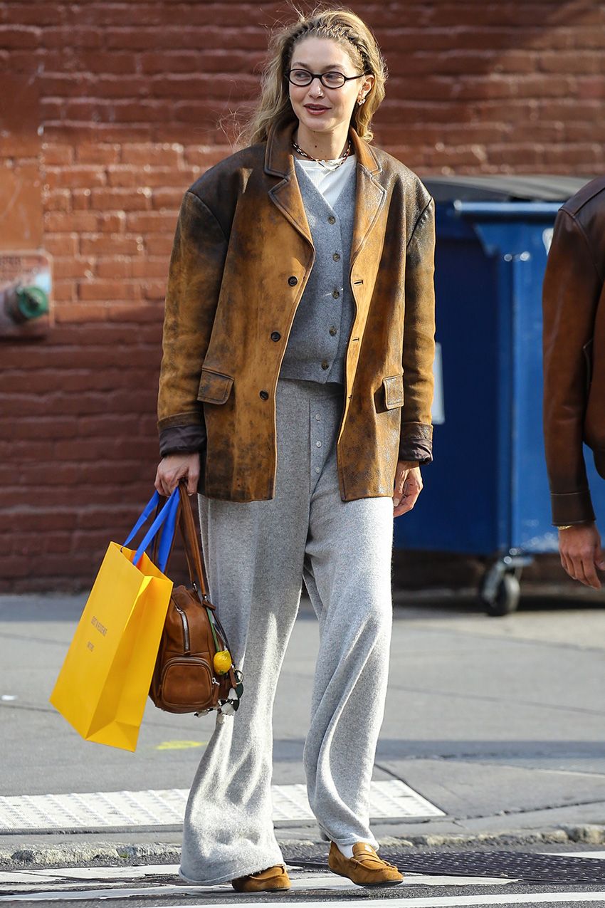 Gigi Hadid wearing a brown leather jacket with a gray cardigan and sweatpants and soft Miu Miu loafers