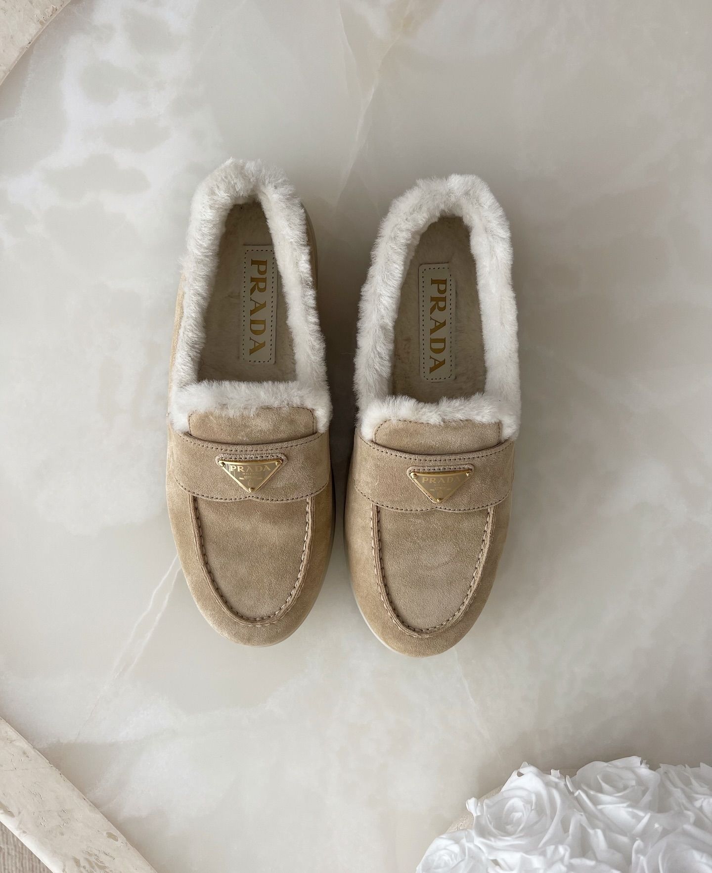 @lovisabarkman showcases a pair of beige suede shearling loafers from Prada on a marble surface