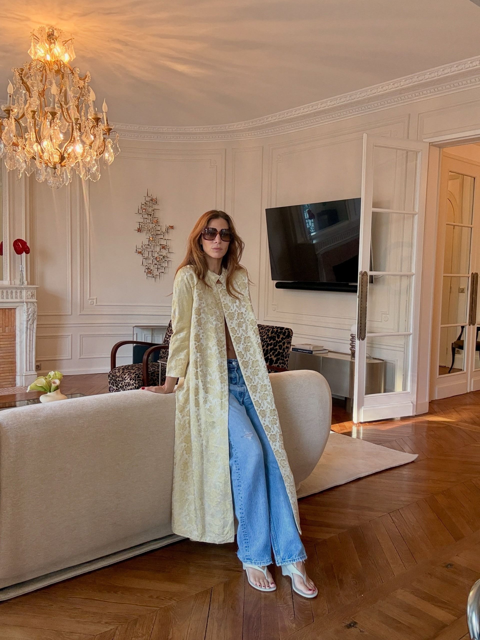 An image of @jen_wonders wearing an ornate coat with blue jeans and white wedge heels.