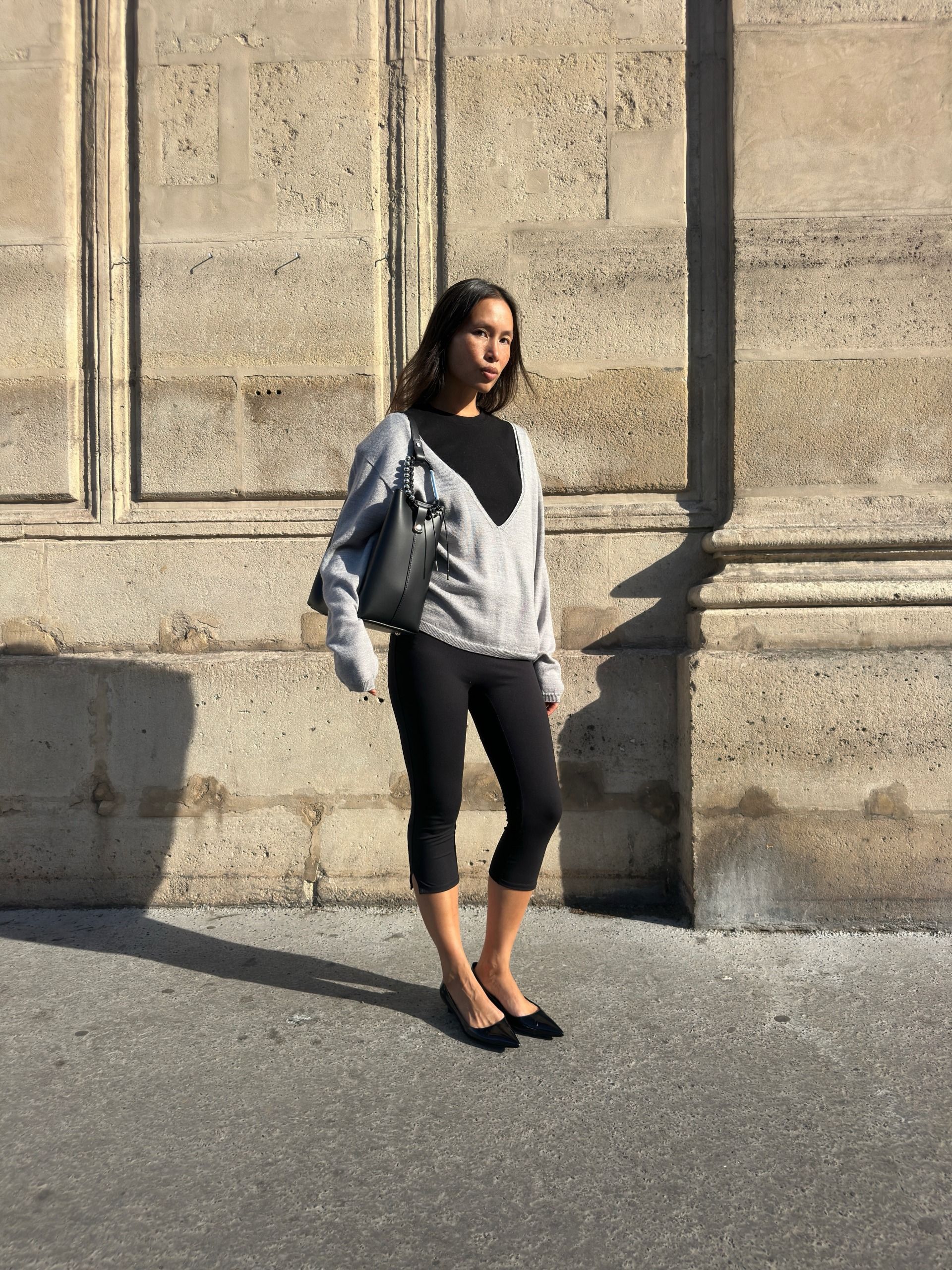An image of @vikilefevre  wearing a black t-shirt, grey v-neck jumper and capri leggings.
